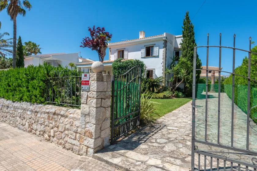 A gated property entrance with a stone wall, greenery, and a paved path.