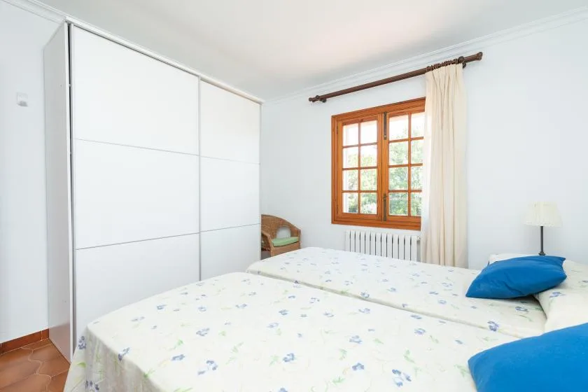 A bright bedroom with beds, a window, and a white wardrobe.