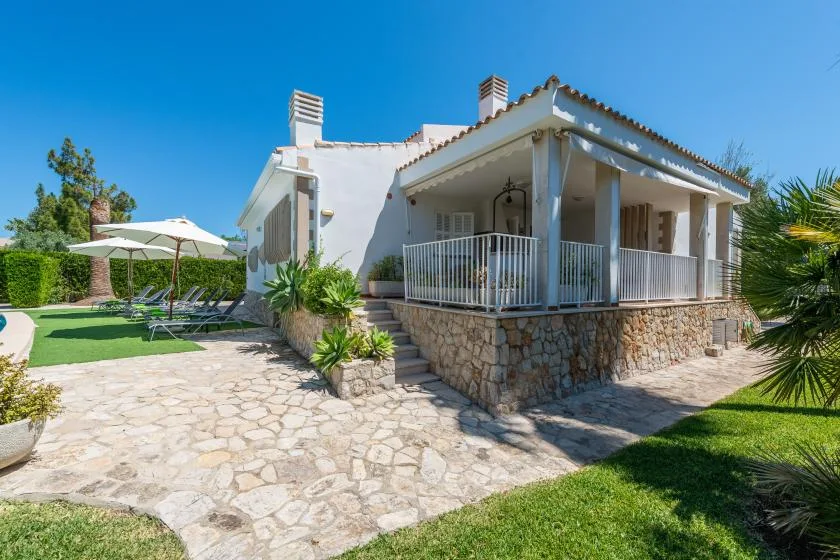 A white house with a covered porch, stone paving, and a landscaped garden.