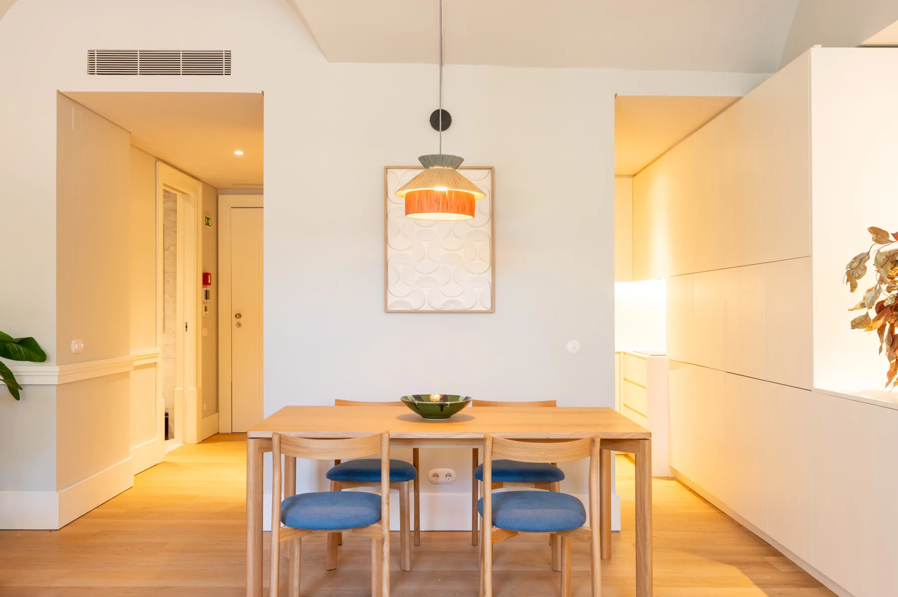 A dining area with a wooden table, blue seating, and a pendant light.