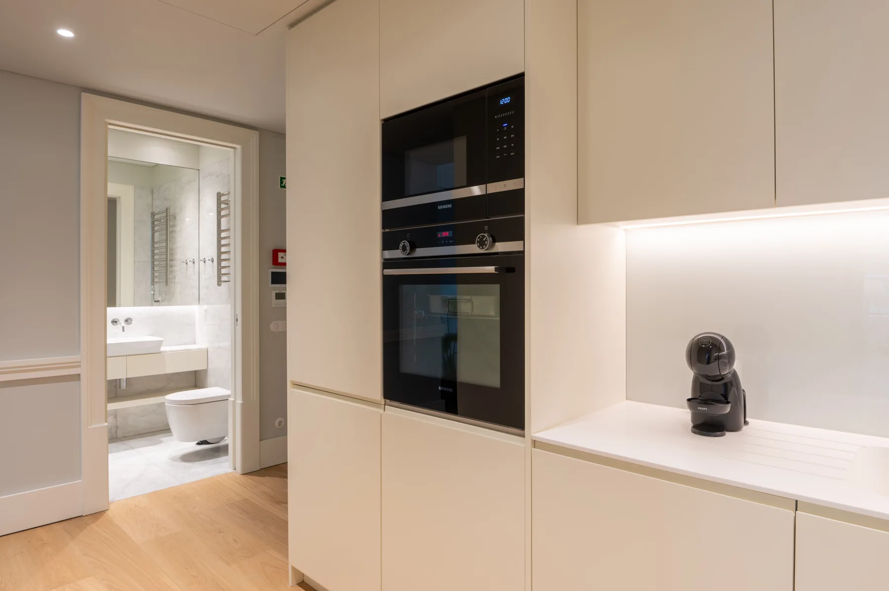 A modern kitchen with built-in appliances and a doorway to the bathroom.