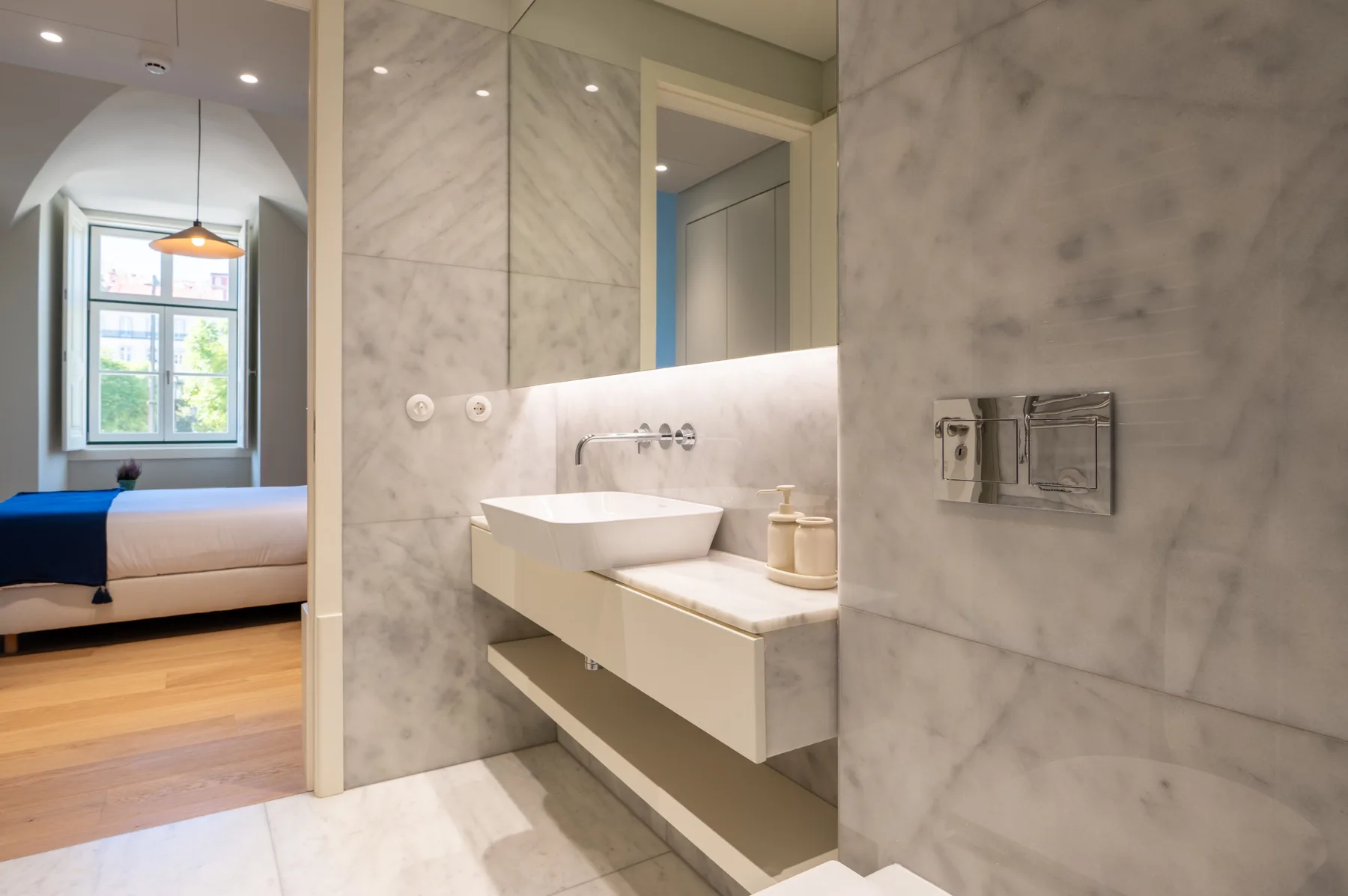 A modern bathroom with a floating sink and a view into a bedroom.