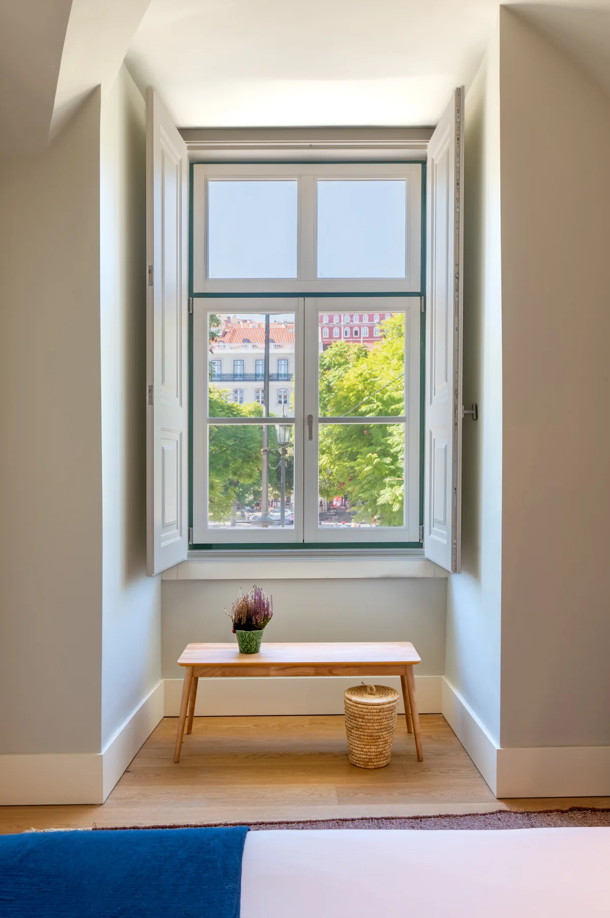 A bright window alcove overlooks leafy trees, with a wooden bench beneath the window.