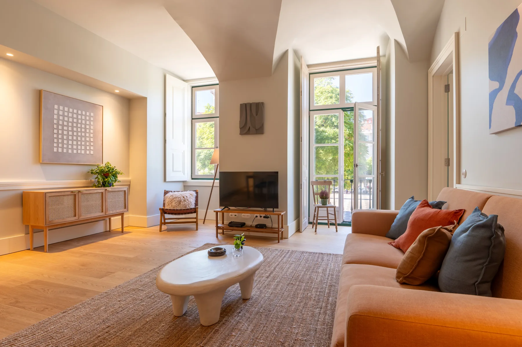 A bright living room with seating, a television, and tall windows.
