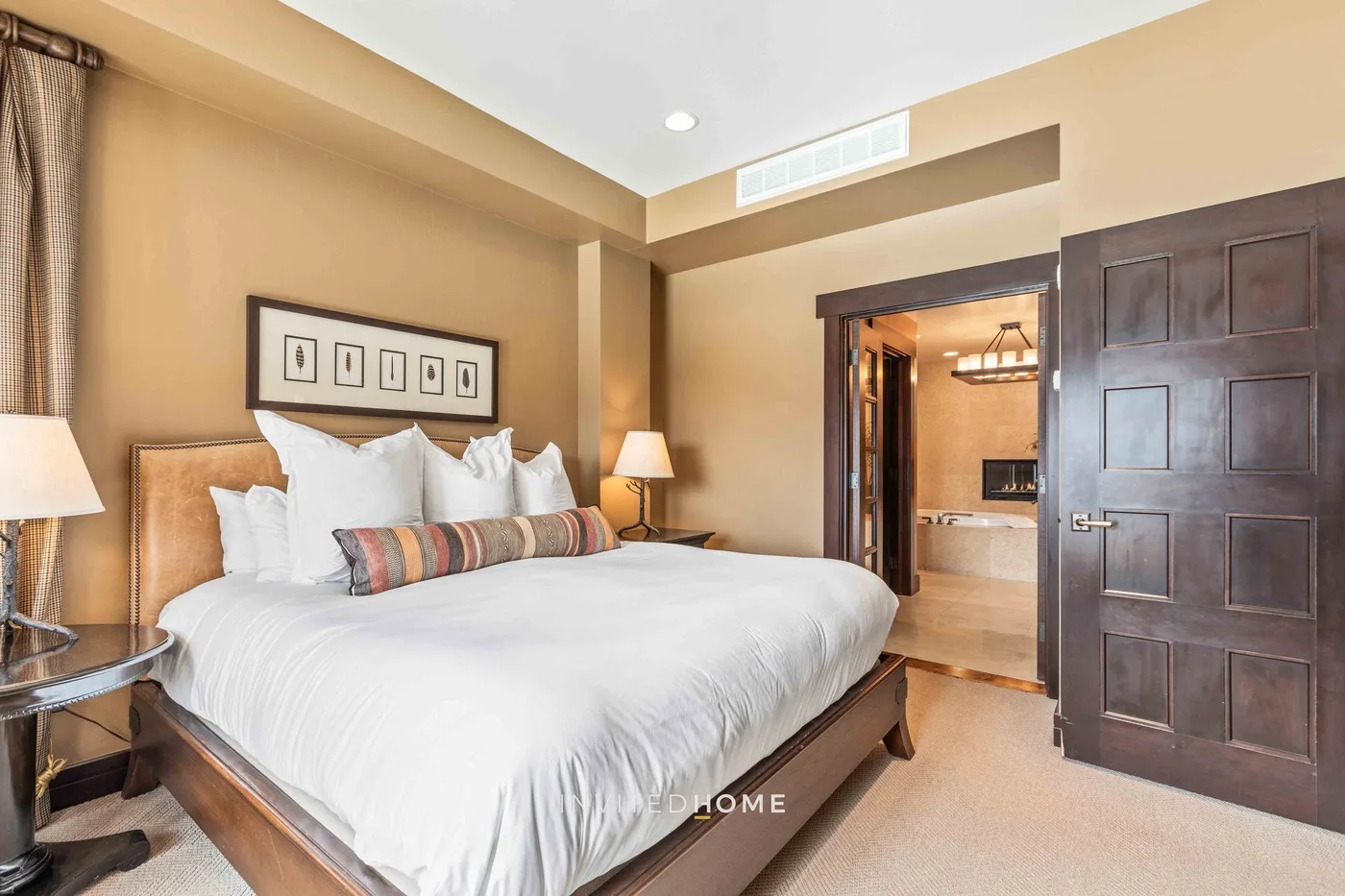 A bedroom with a large bed, framed artwork, and an open doorway.