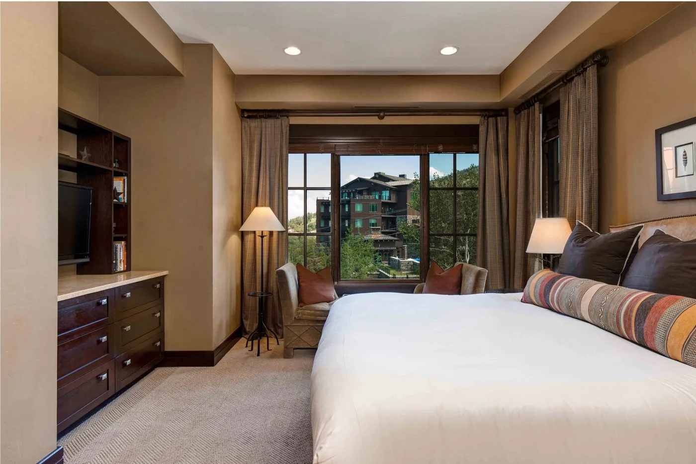 A bedroom with a large bed facing a window and a small seating area.