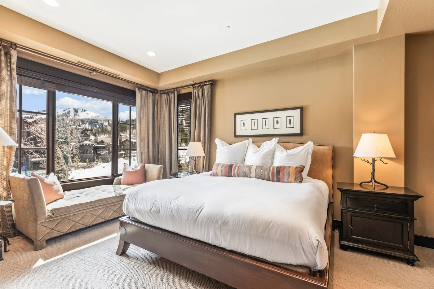 A bedroom with a large bed, bedside tables, and windows overlooking a snowy landscape.