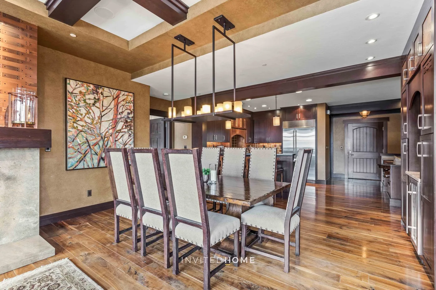 A dining area with a long table, upholstered seating, and a large abstract painting.