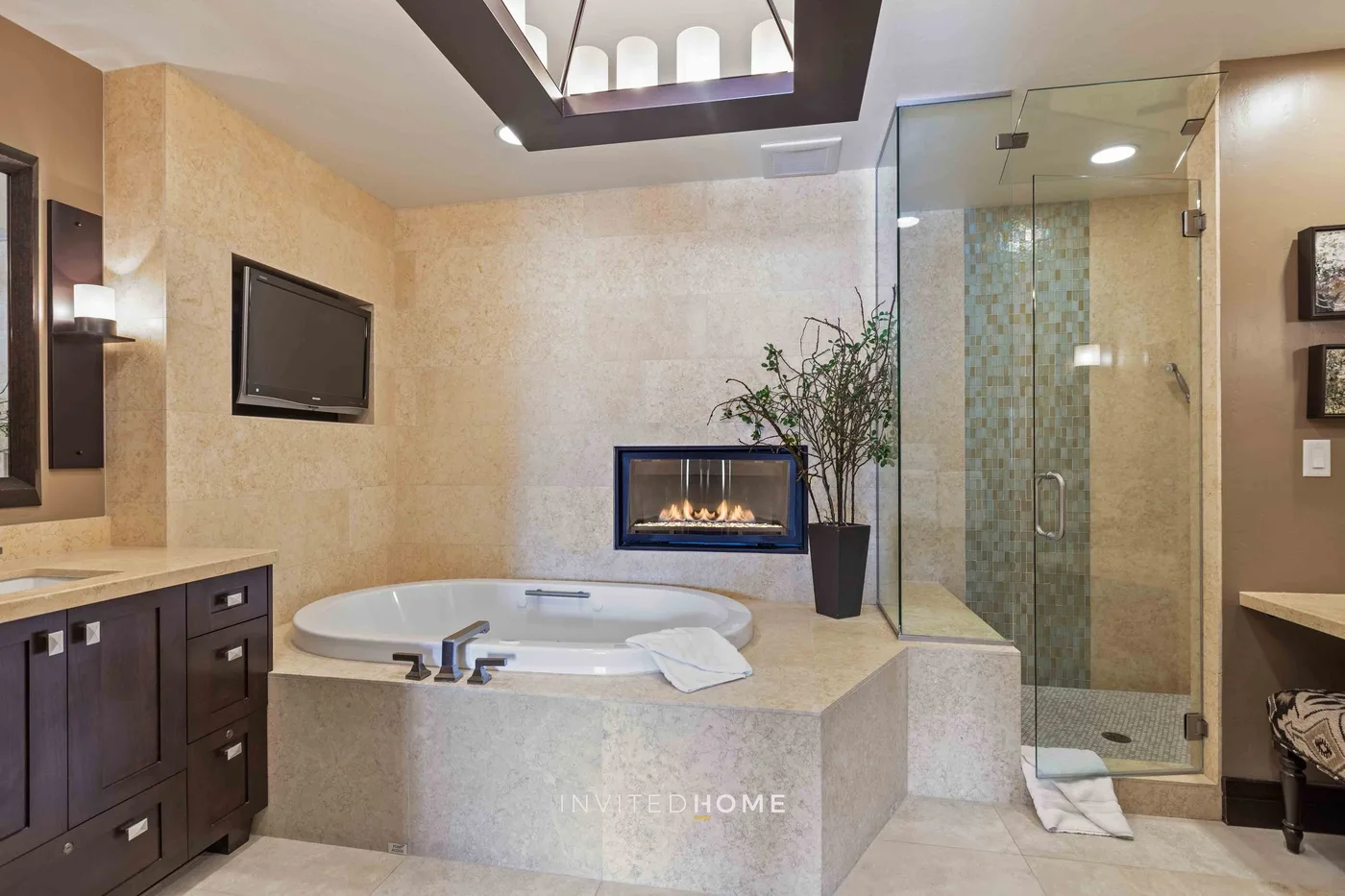 A bathroom with a built-in soaking tub, glass shower, and fireplace.