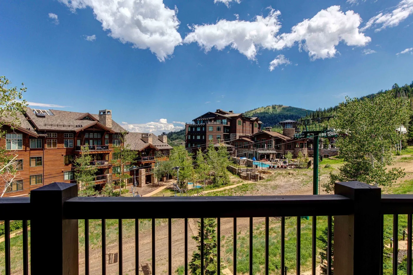 A balcony overlooks a mountain resort complex beneath a blue sky.