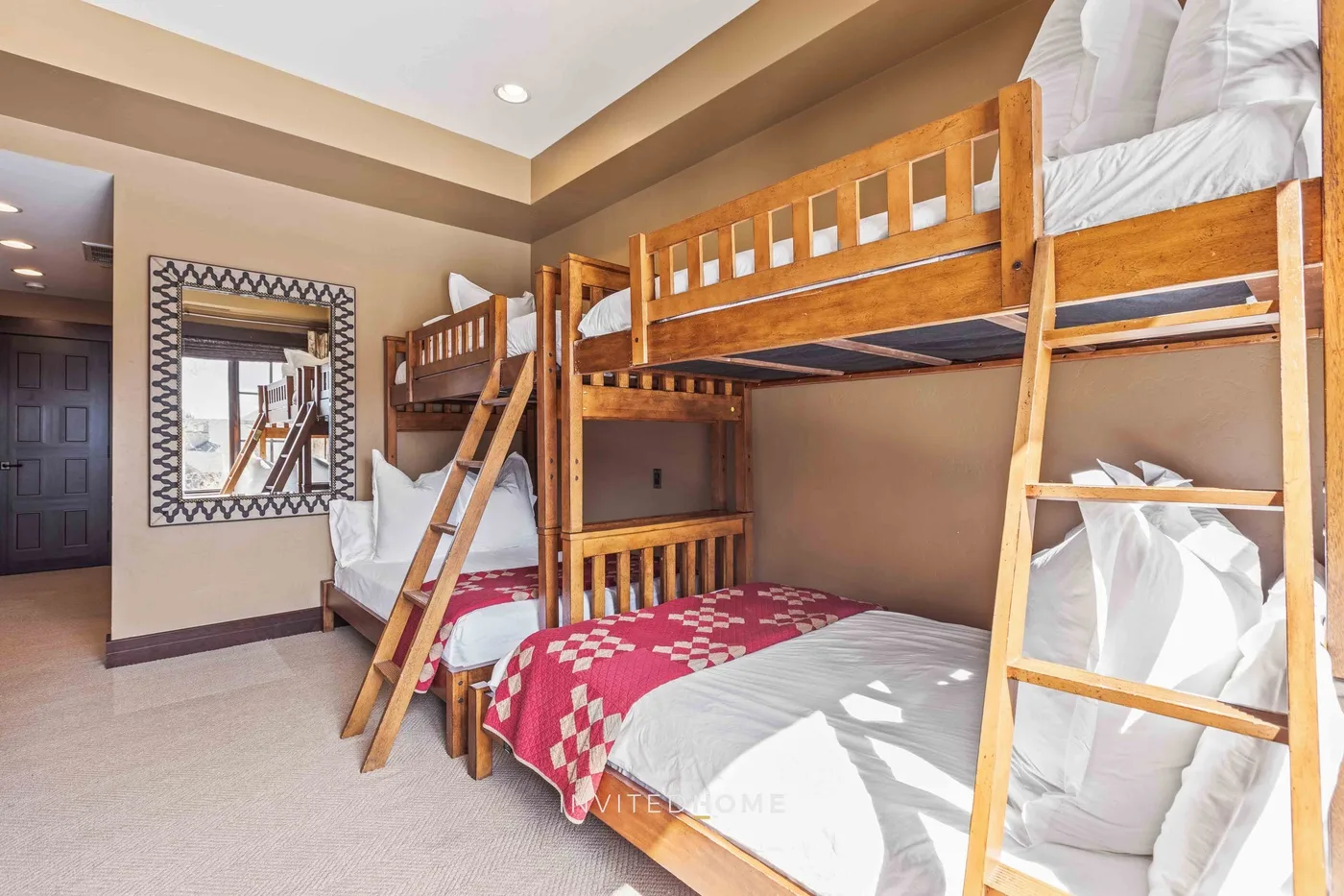 A bedroom with wooden bunk beds, white bedding, and a red patterned blanket.