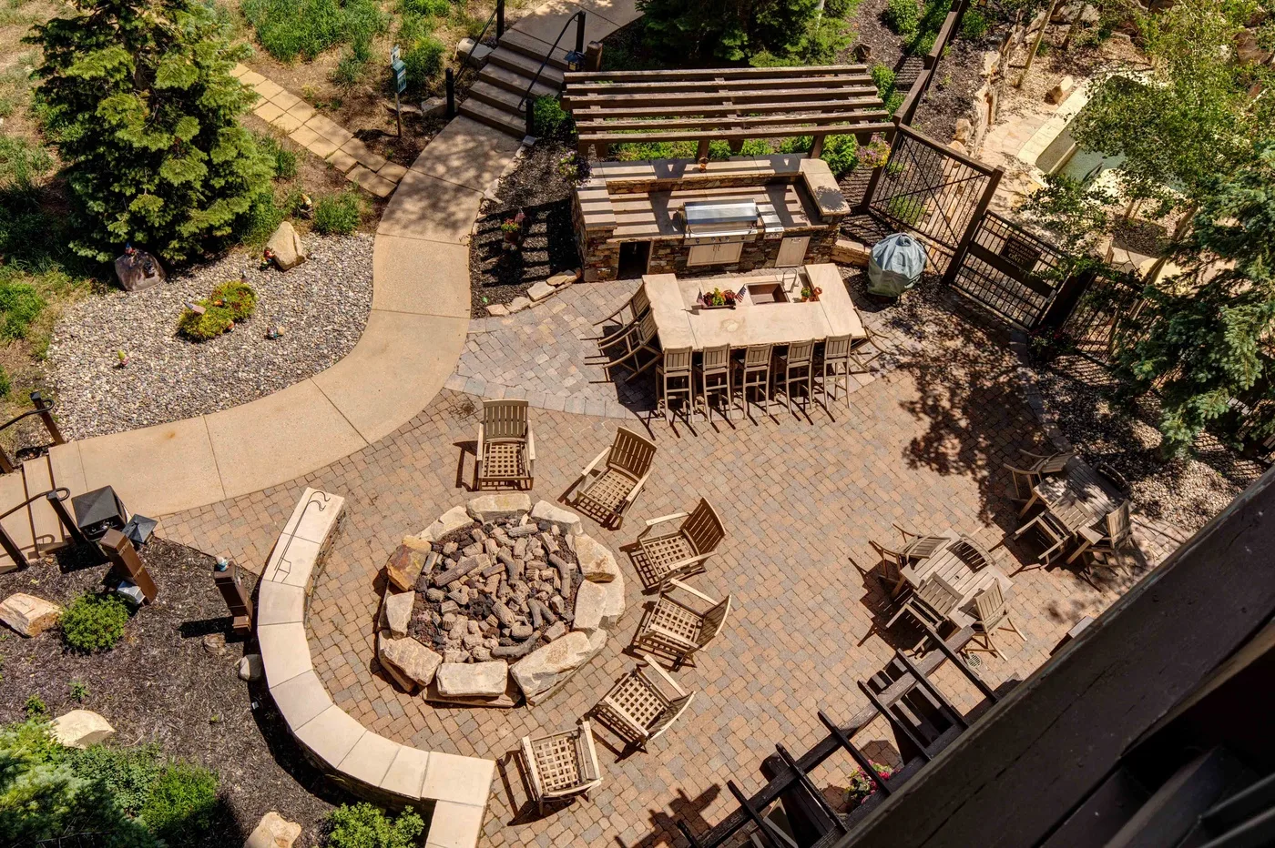 An outdoor patio features a dining table, seating, and a circular stone fire pit.