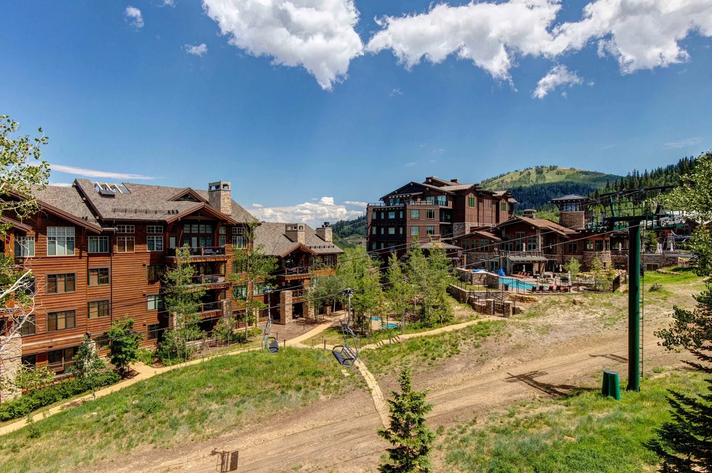 Wooden lodge buildings sit beside a dirt path in a landscaped mountain setting.