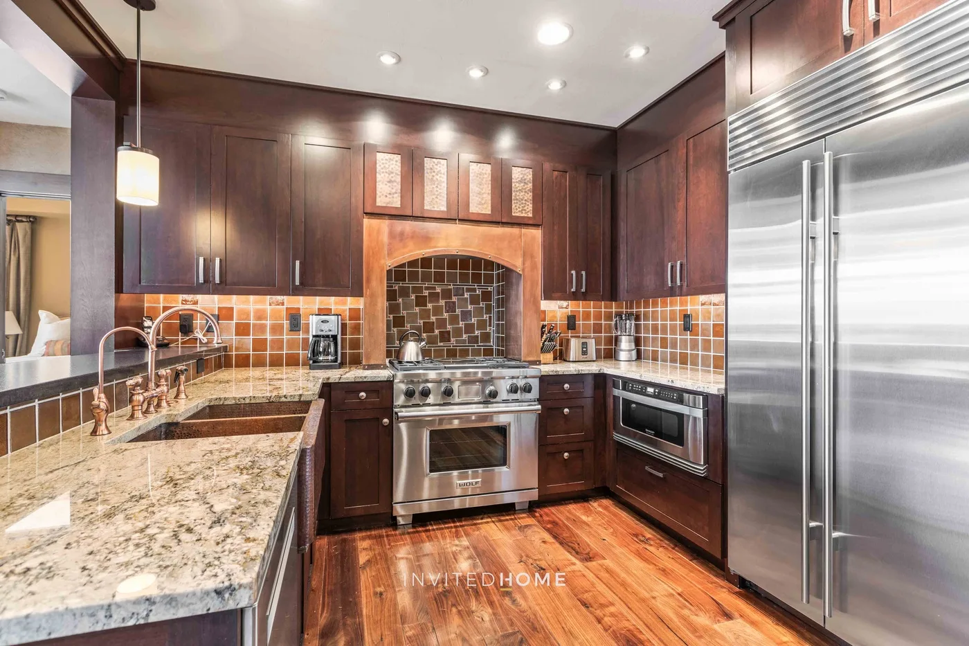 A spacious kitchen with dark cabinetry, stainless steel appliances, and patterned tile backsplash.