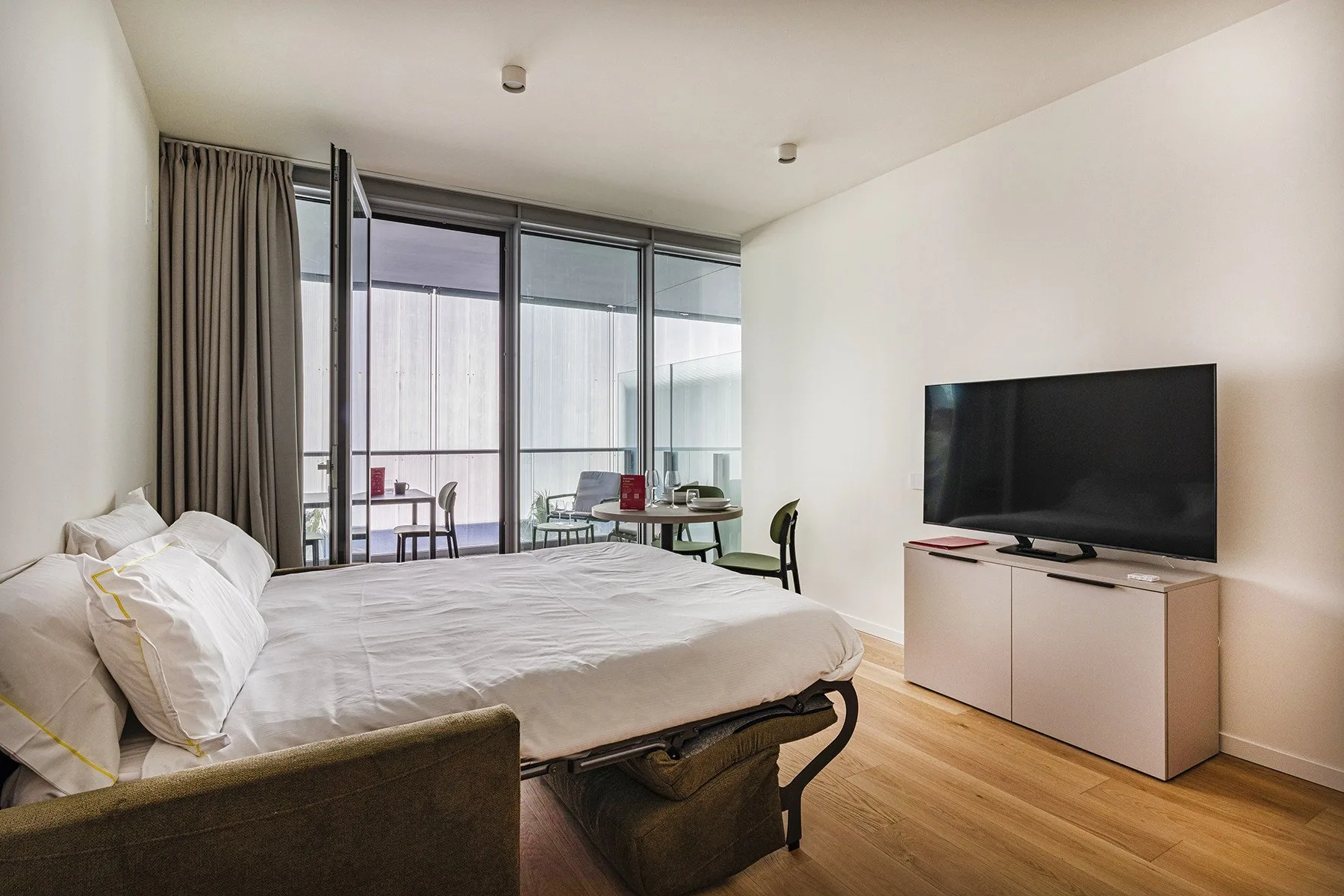 A bedroom with a large bed, floor-to-ceiling windows, and a television.