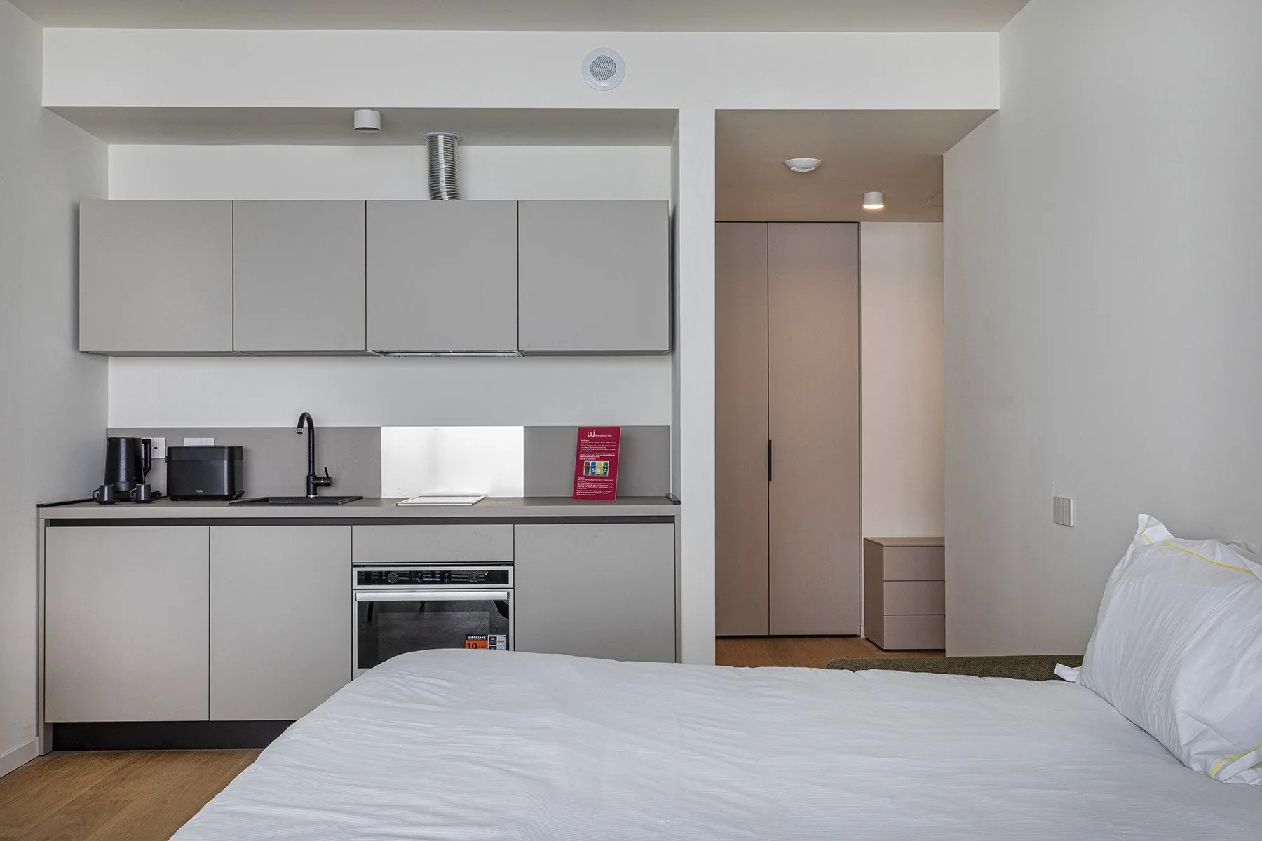 A bedroom with a bed beside a compact kitchenette.