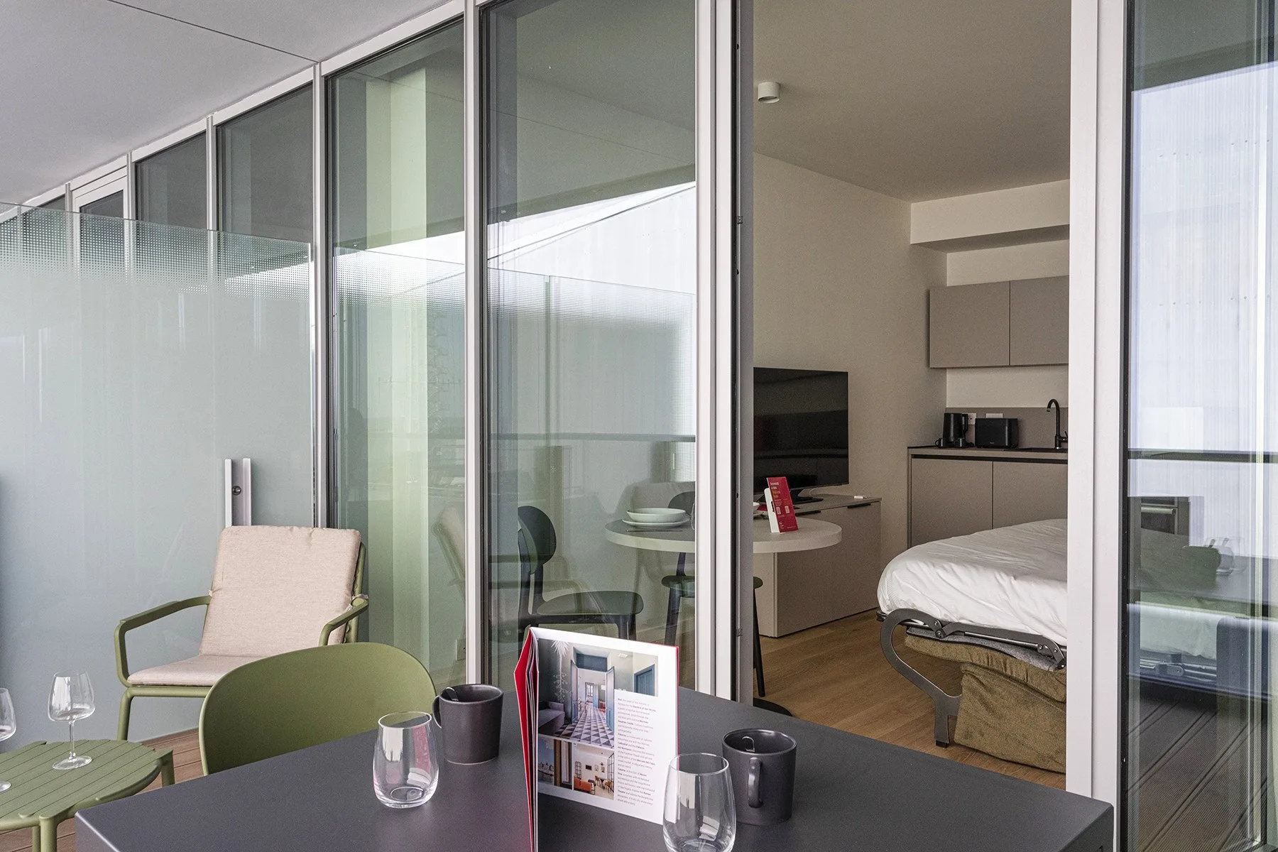 A bedroom with a bed, kitchenette, and glass doors opening onto a balcony.