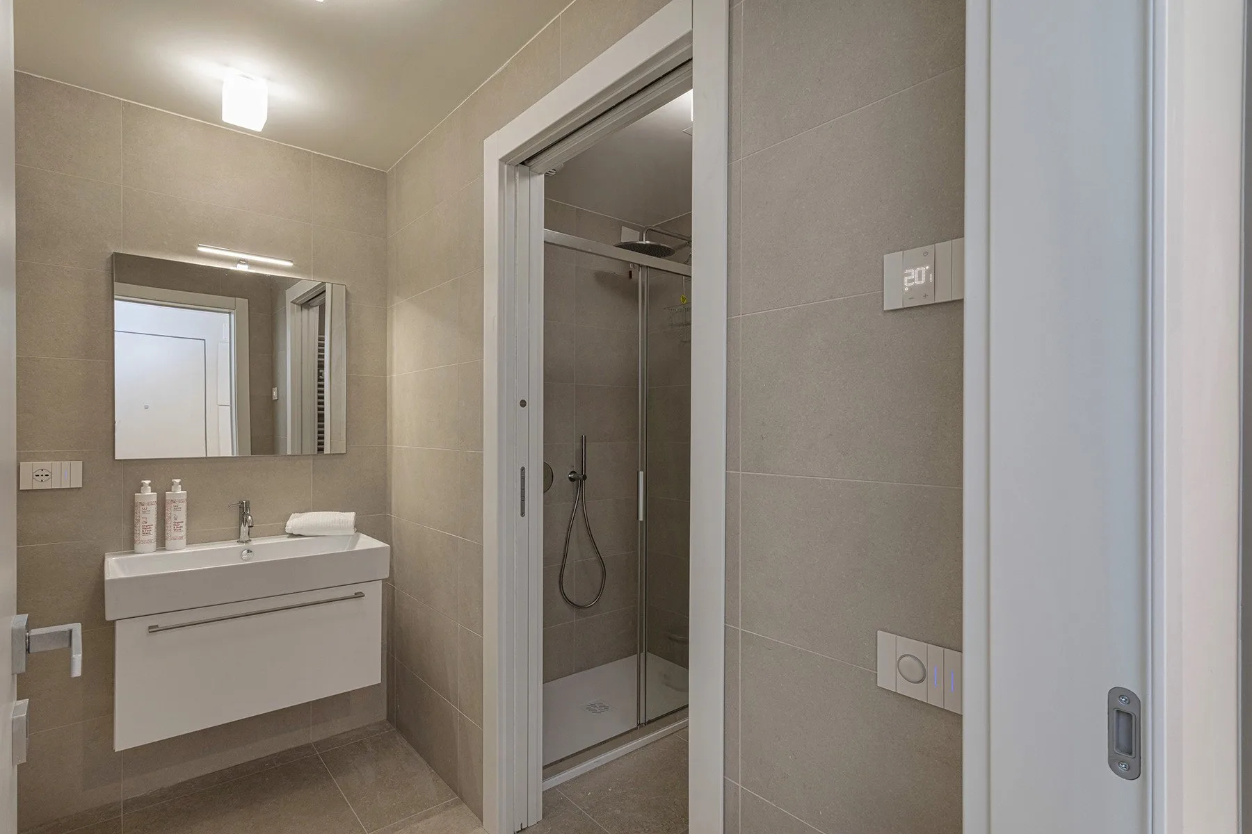 A tiled bathroom with a floating sink and a glass shower.