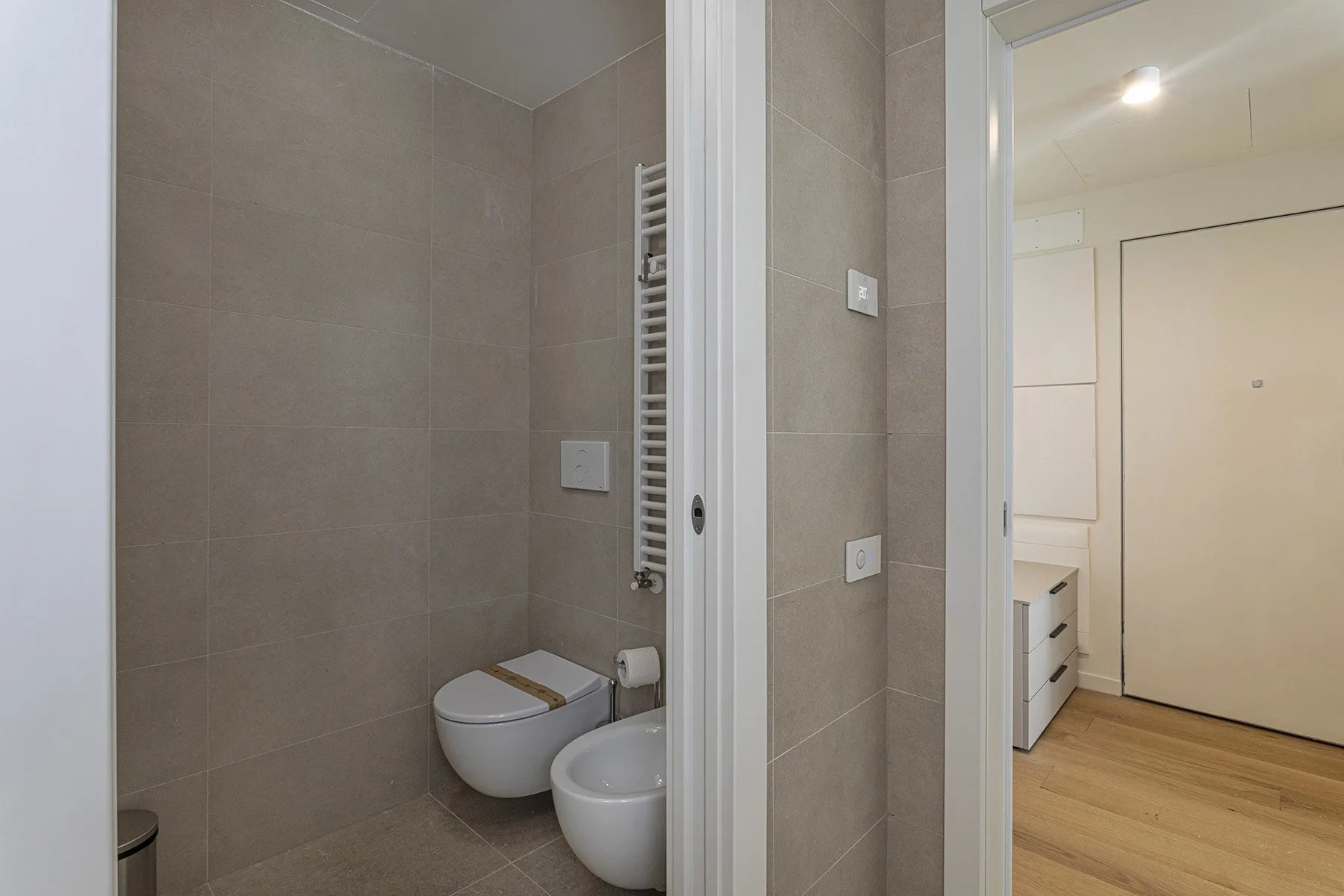 A tiled bathroom with a wall-mounted toilet and a small basin.