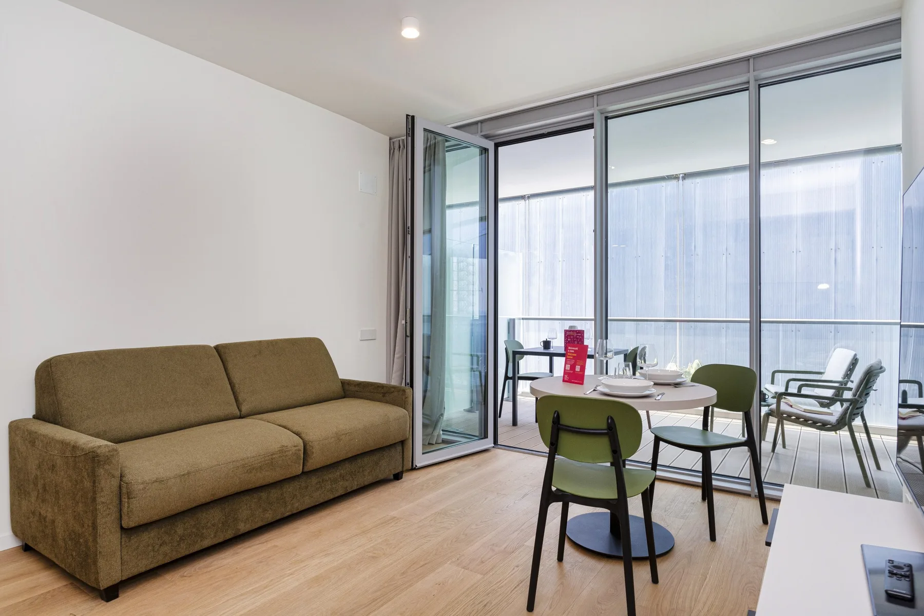 A living and dining area with a sofa, table, and large glass windows.
