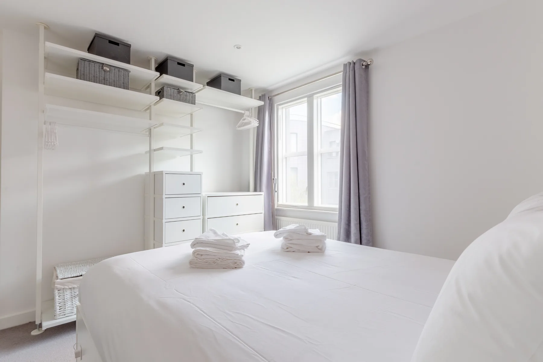 A bright bedroom with a white bed, open shelving, and a window.
