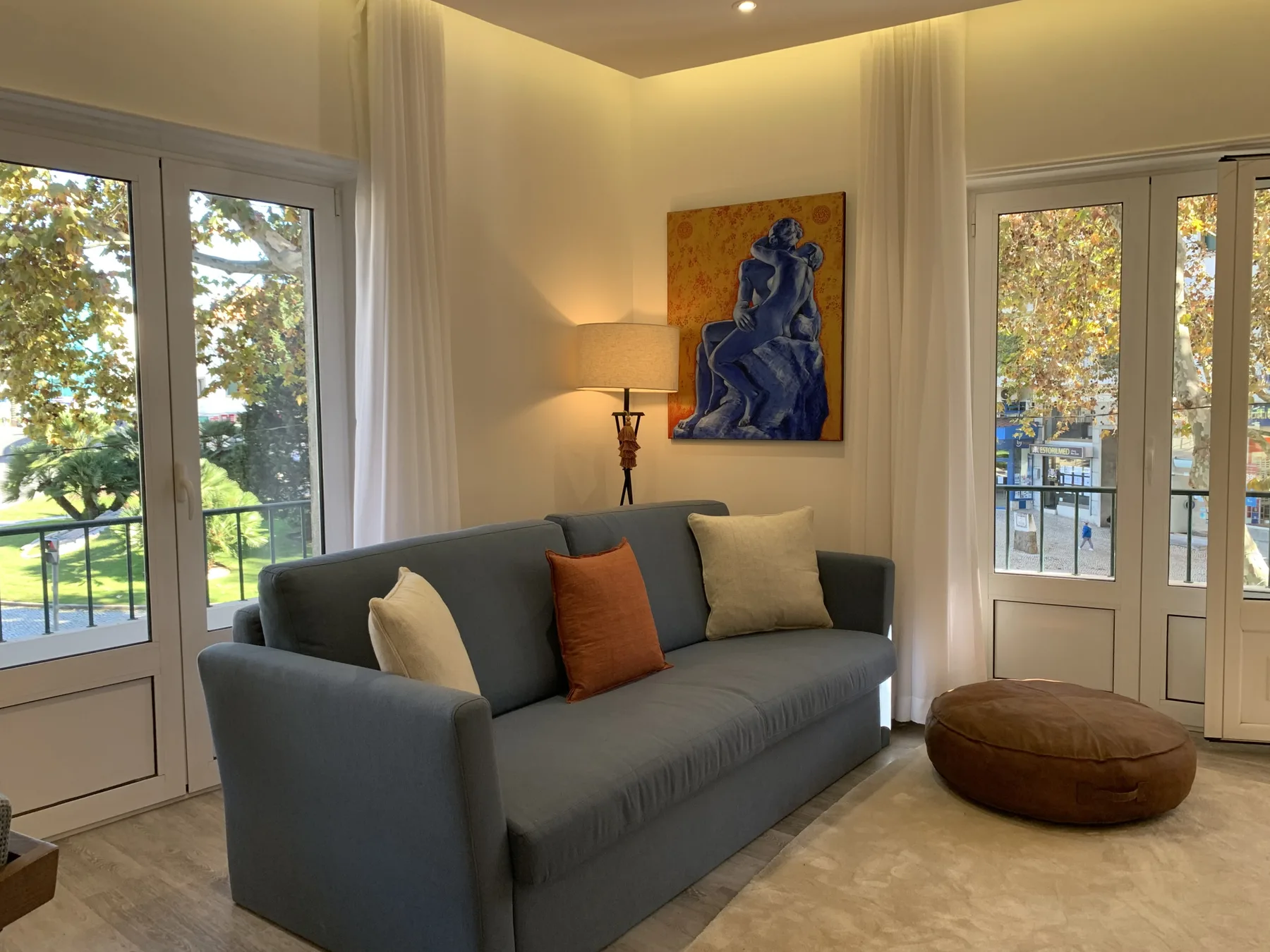 Una sala de estar con un sofá gris, una lámpara de pie y una ventana grande.