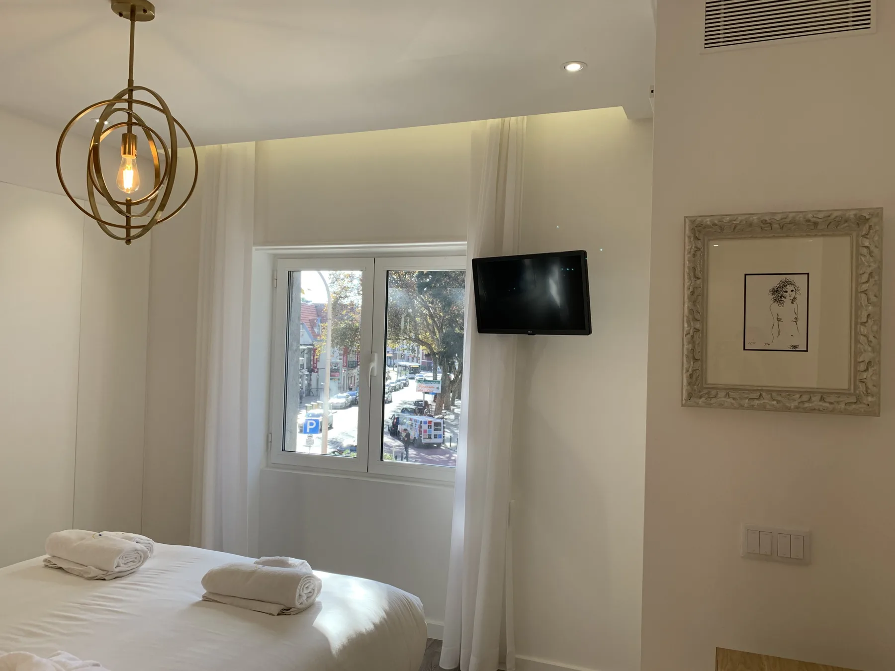 Un dormitorio con cama, ventana y televisor montado en la pared.
