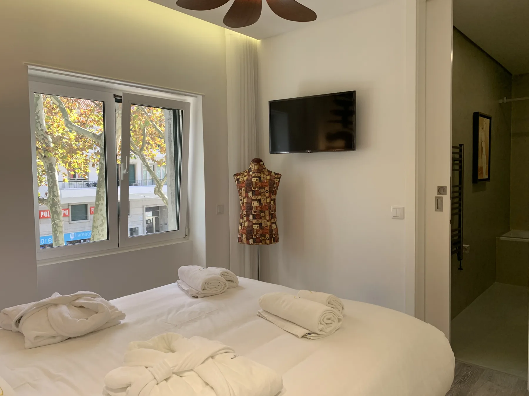 Dormitorio con una cama tendida, una ventana y un televisor en la pared.