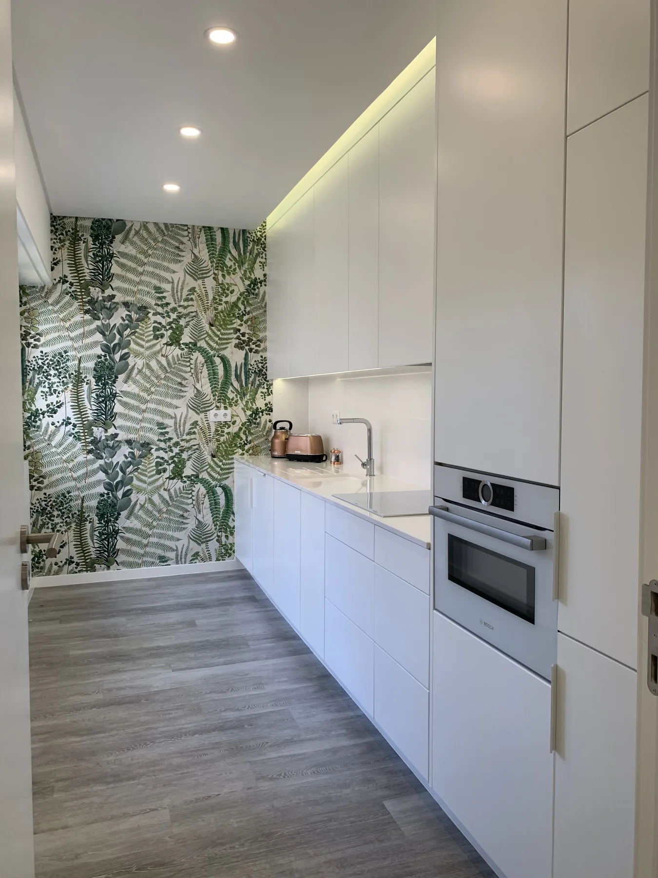 Una cocina moderna con gabinetes blancos y papel tapiz de hojas.