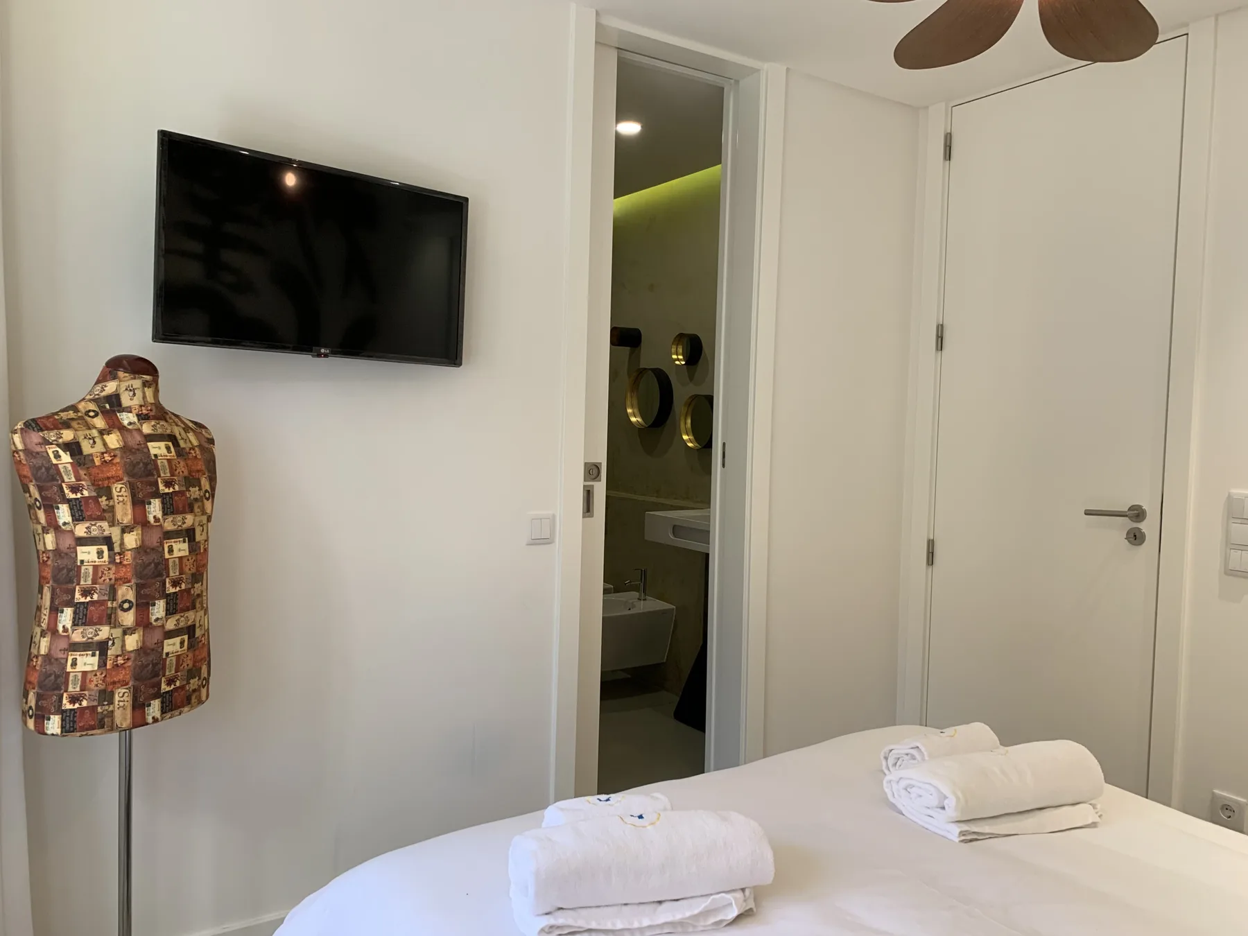 Un dormitorio con un televisor en la pared y la puerta del baño abierta.