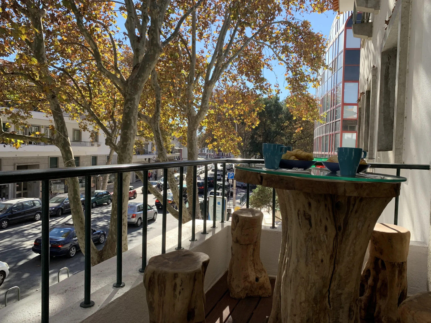 Una zona de estar en el balcón da a una calle arbolada con coches estacionados.