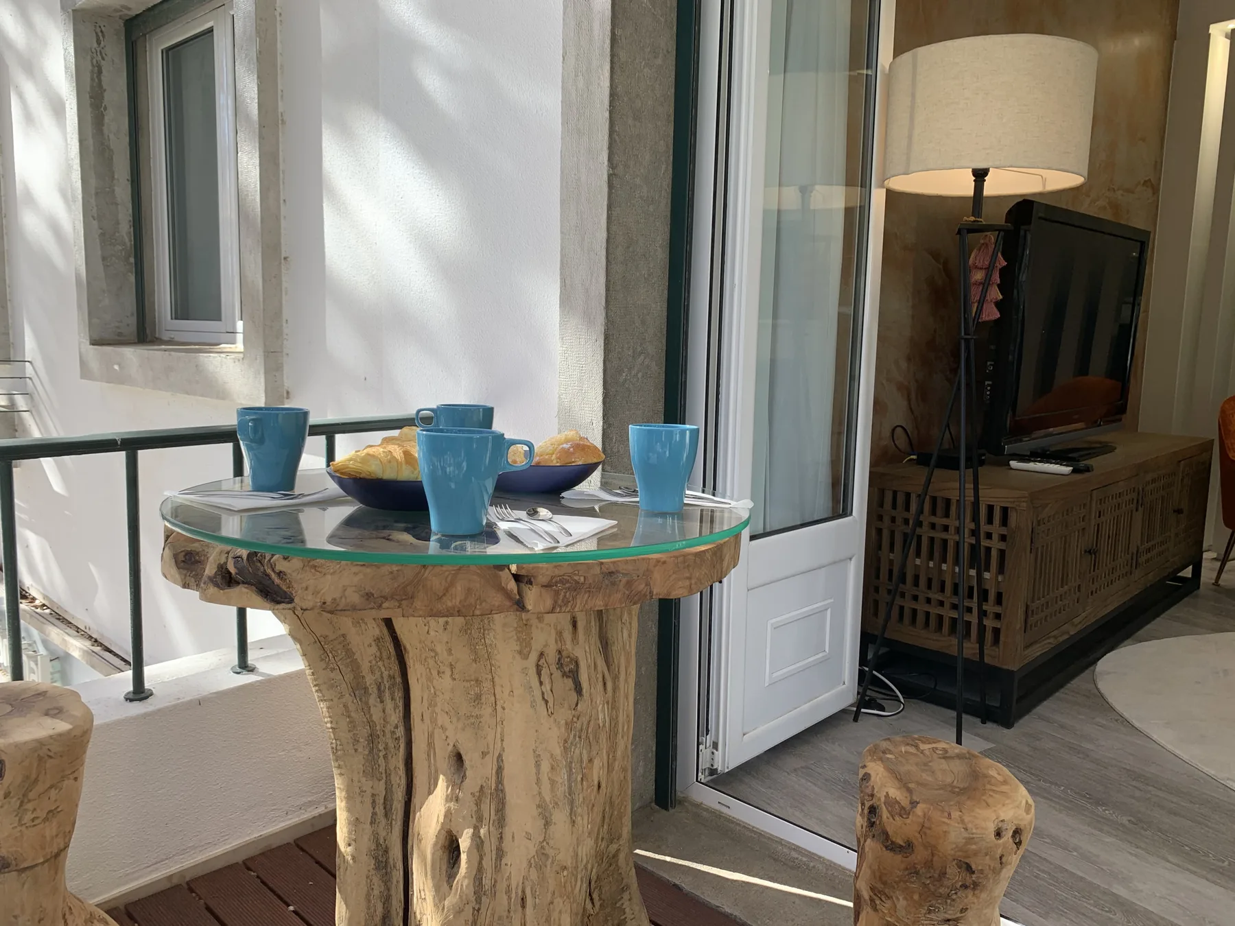 Una pequeña zona de estar con una mesa de vidrio, televisor y lámpara de pie.