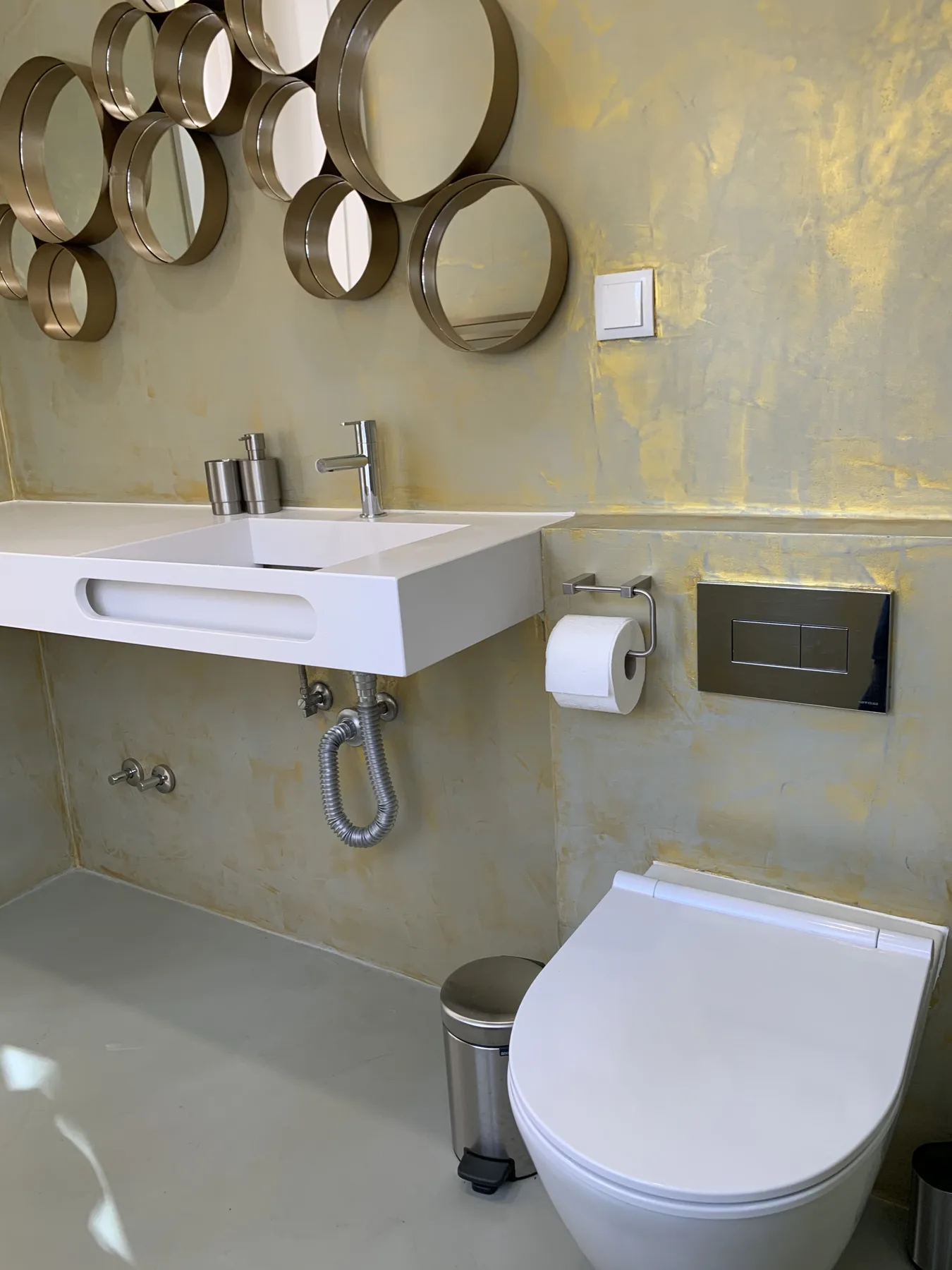 Un baño con lavabo suspendido e inodoro bajo espejos redondos.