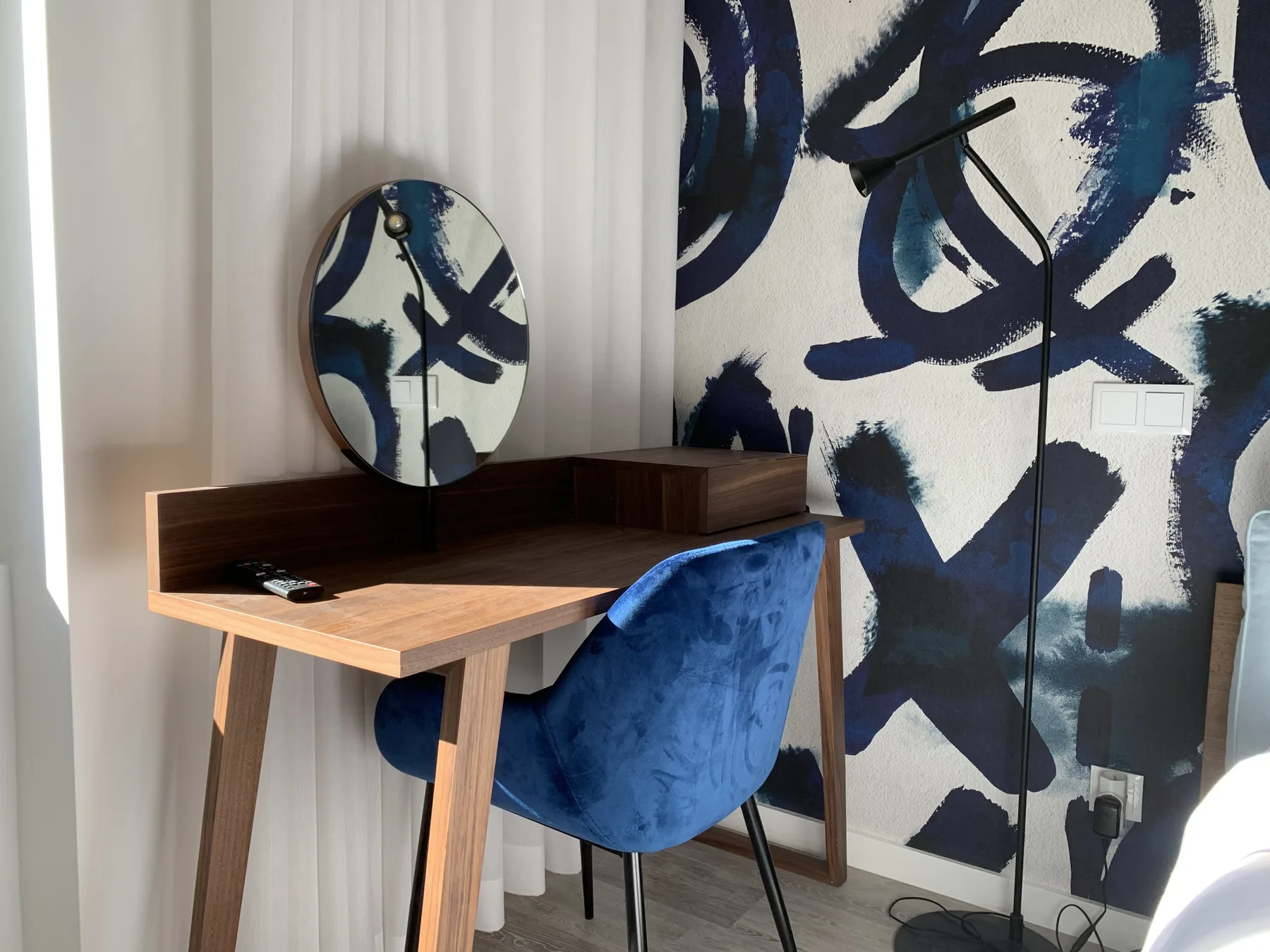 Un pequeño escritorio y asiento azul están junto a un llamativo mural abstracto.