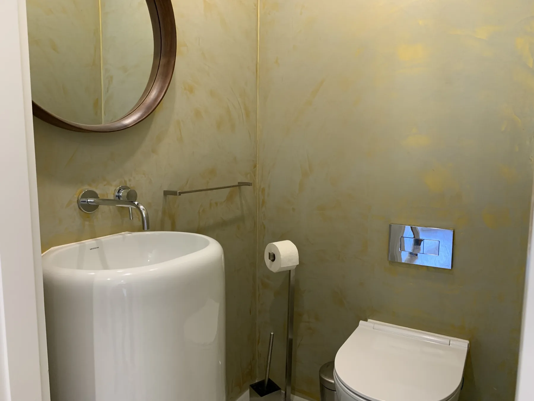 Un baño con lavabo, inodoro y placa de descarga en la pared.