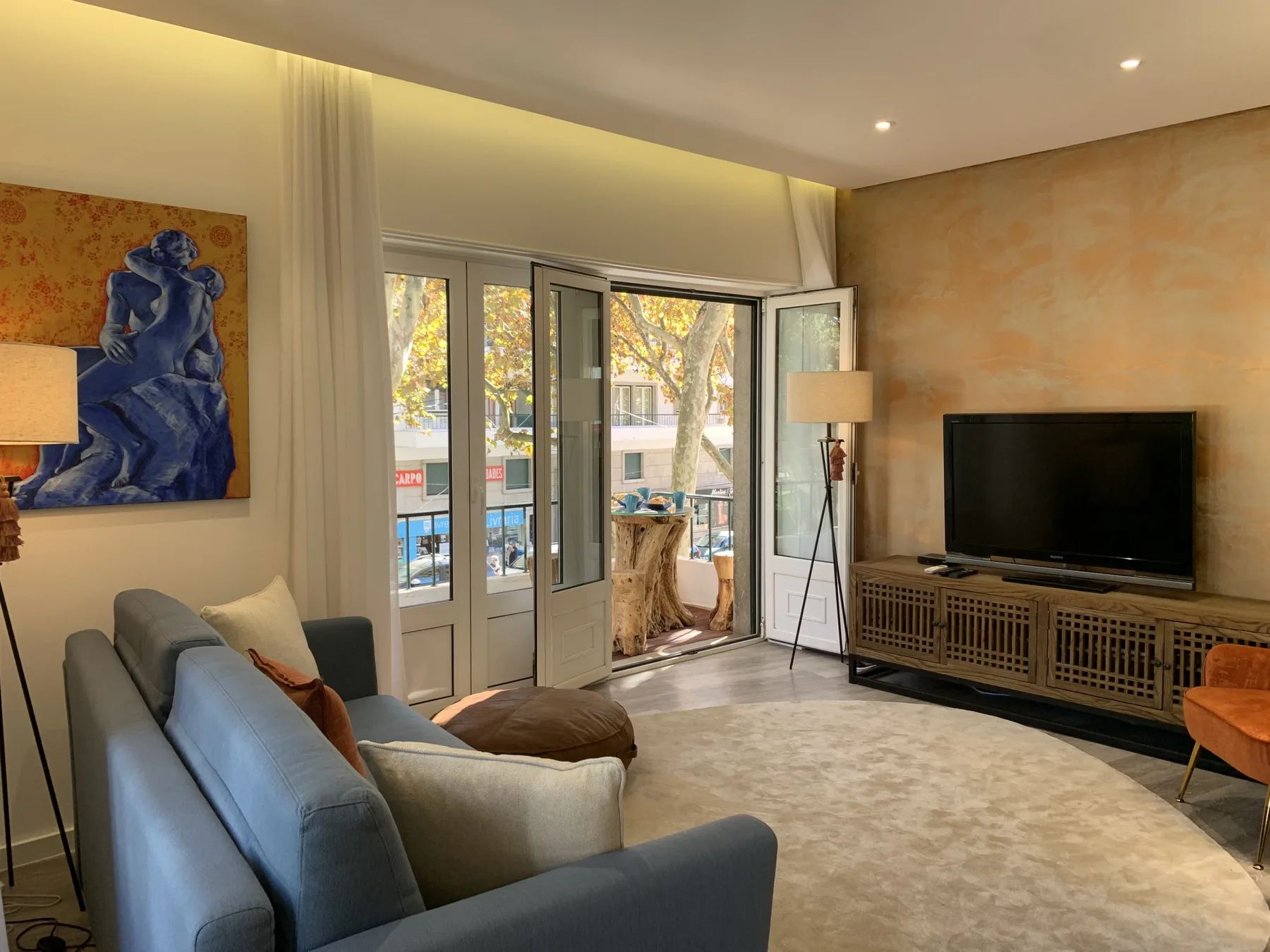 Sala de estar con asientos, un televisor y puertas abiertas a un balcón.