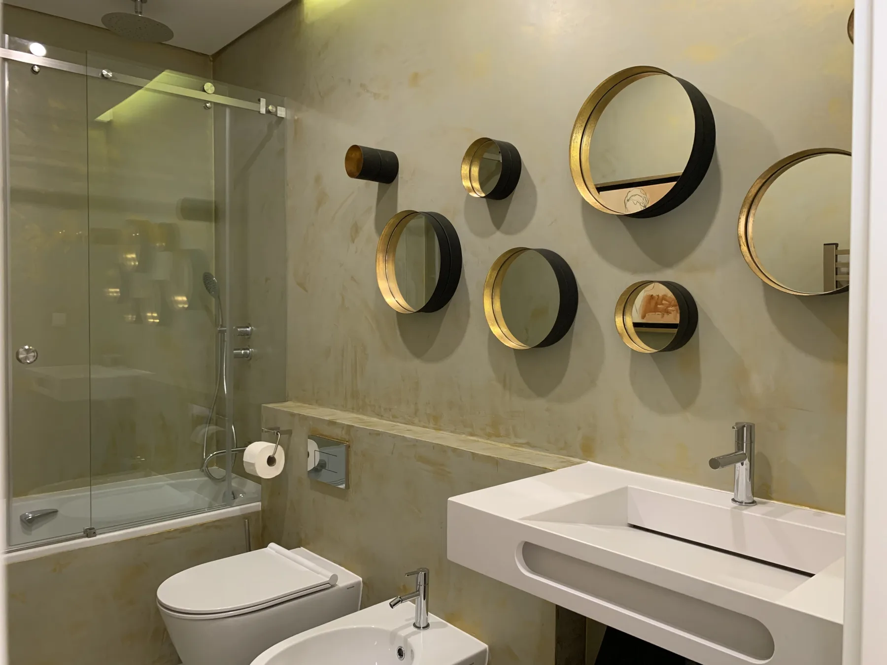 Un baño moderno con ducha de vidrio, inodoro y espejos en la pared.