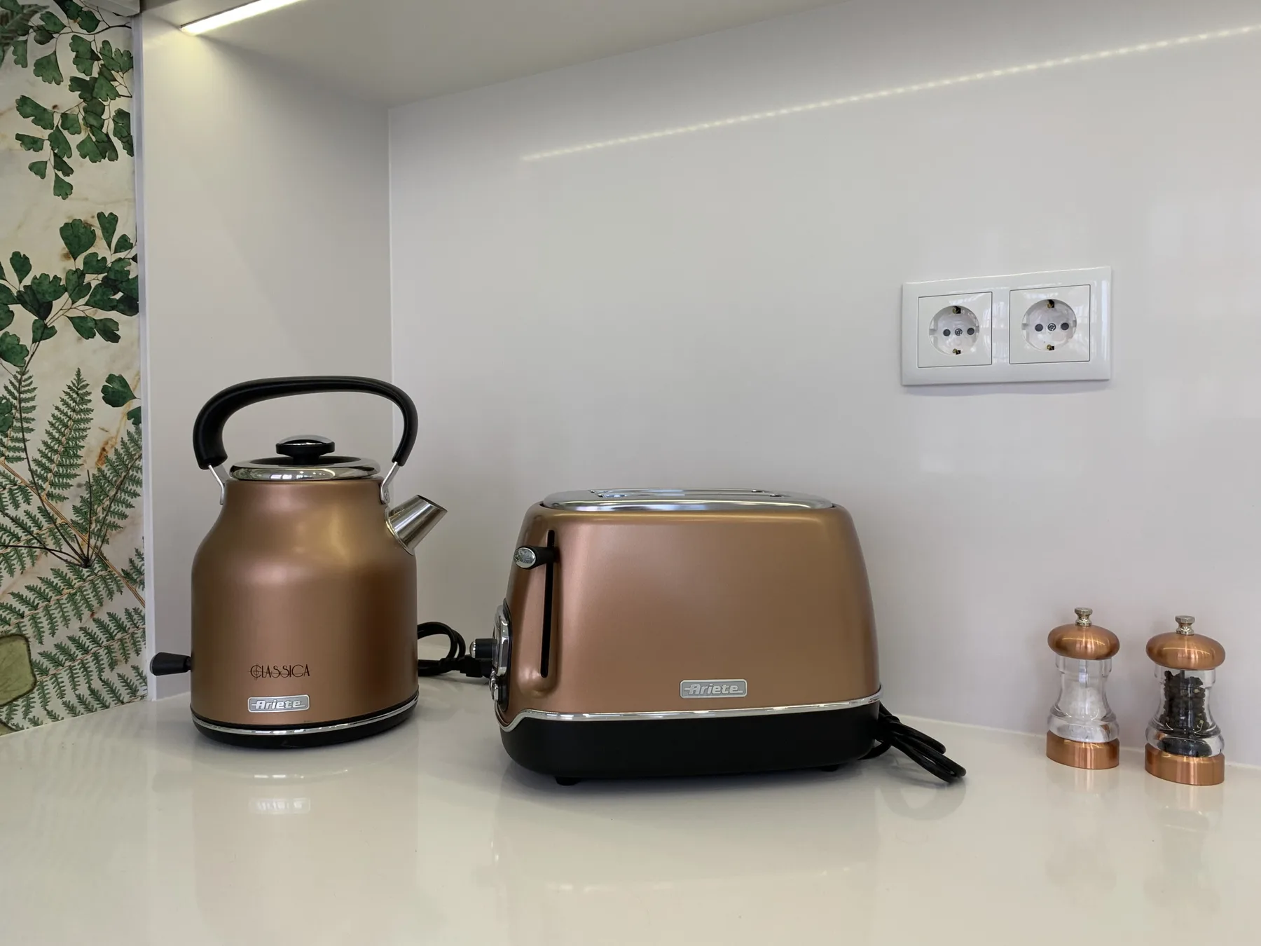Una encimera de cocina con hervidor, tostadora y pequeños molinillos de especias.