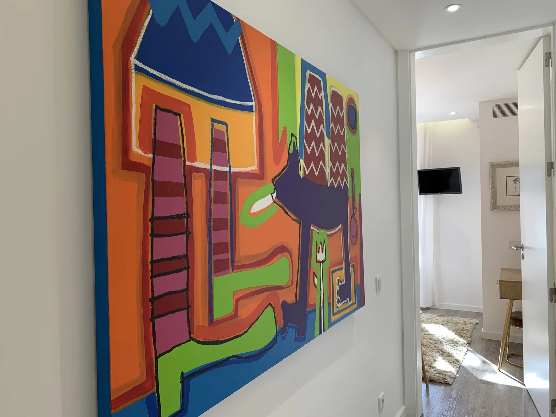 Un pasillo muestra una gran pintura abstracta y colorida junto a una puerta abierta.