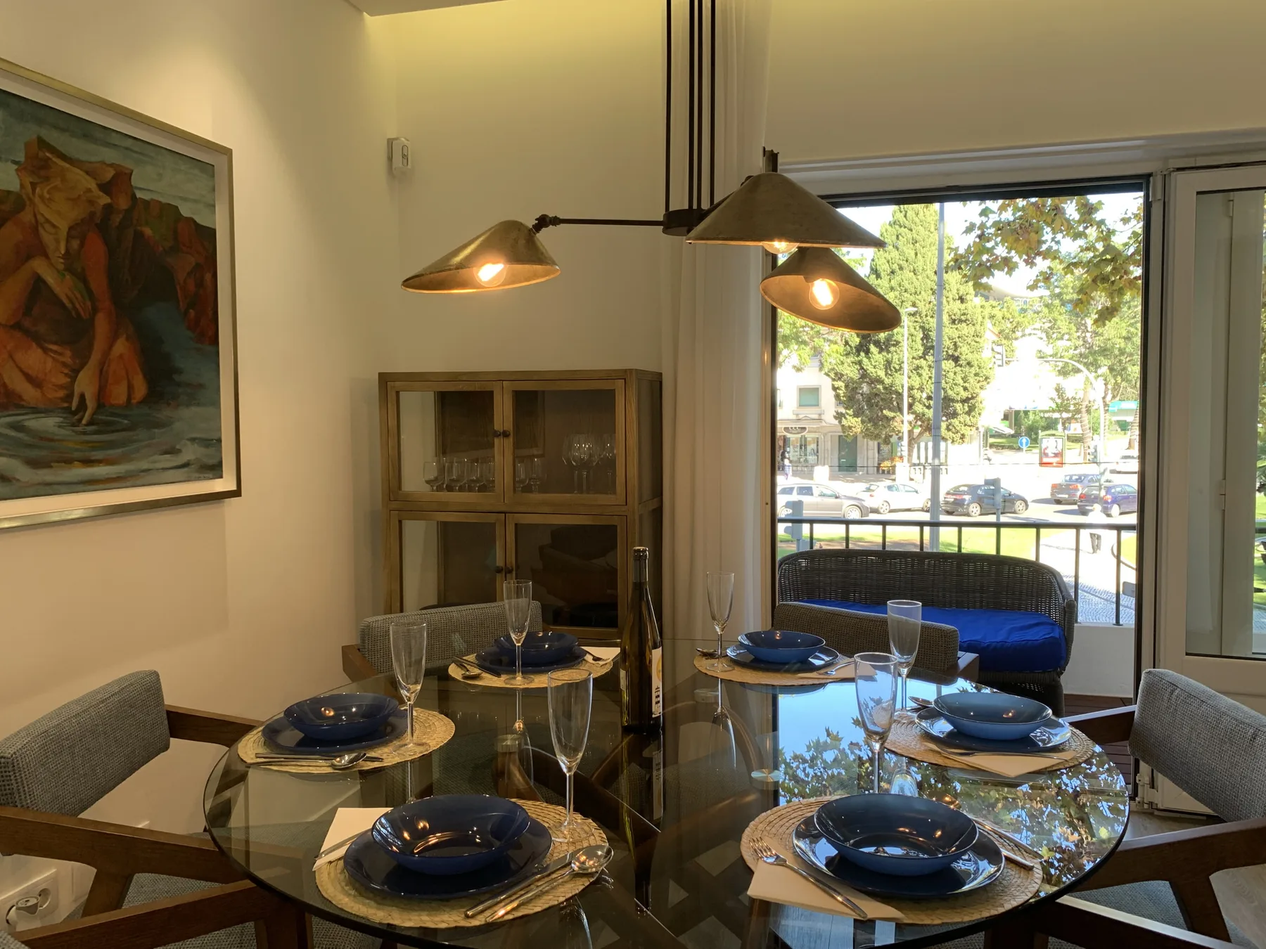 Comedor con una mesa de cristal preparada con platos azules junto a una ventana amplia.
