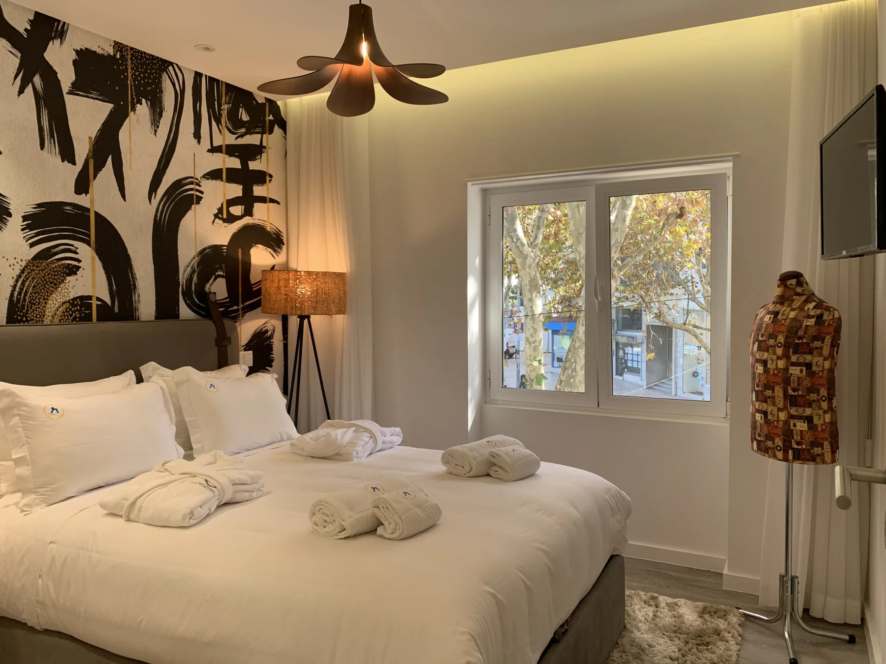 Un dormitorio con una cama grande, arte mural estampado y una ventana con vistas a los árboles.