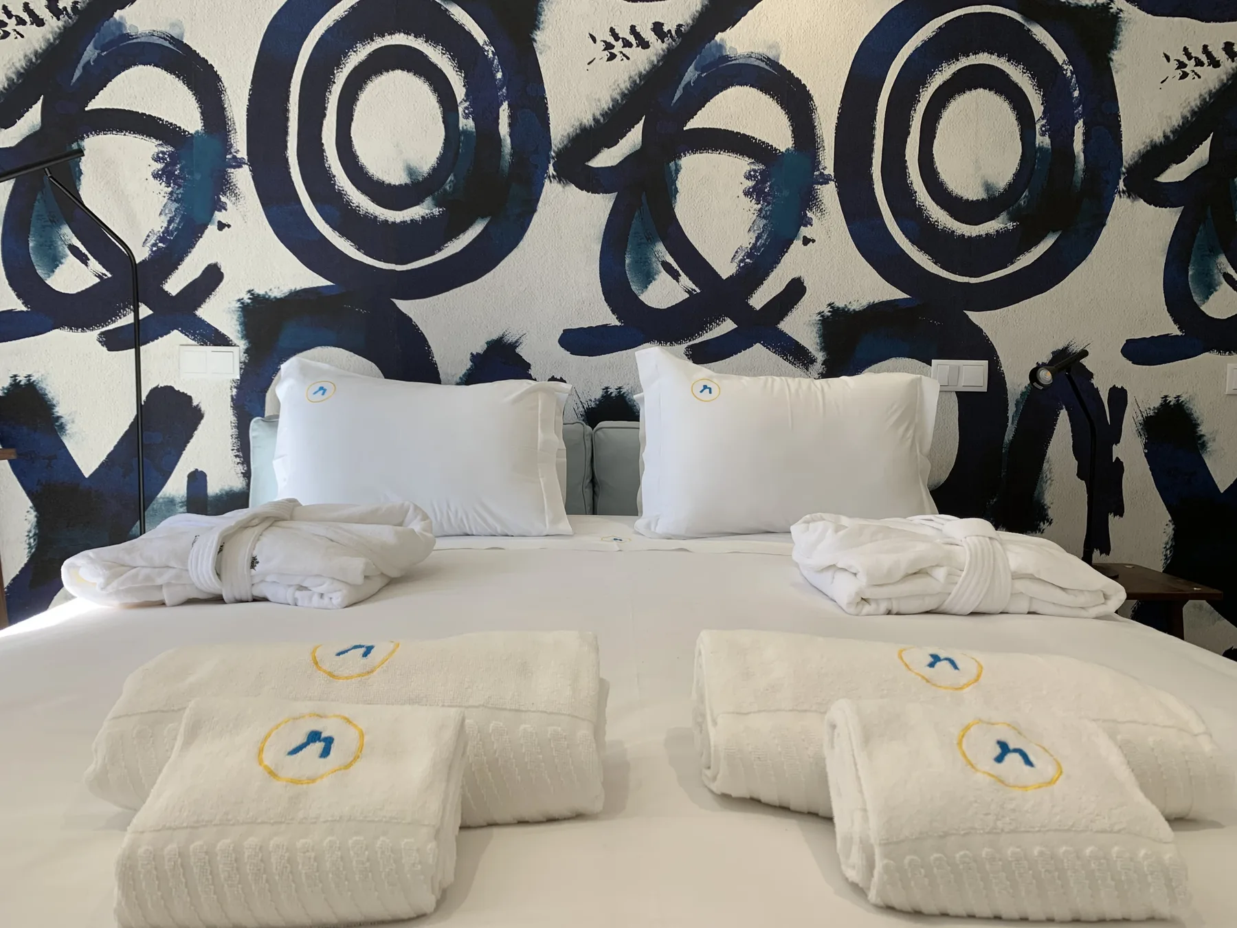 Un dormitorio con una cama bien tendida y toallas frente a un mural abstracto llamativo.