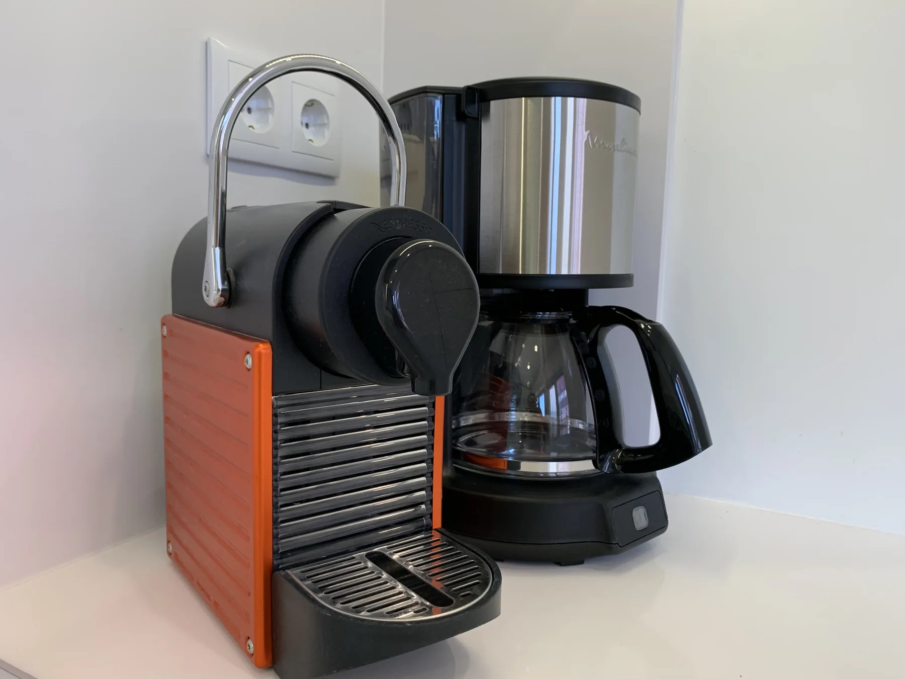 Una estación de café con una cafetera espresso y una cafetera de filtro está sobre una encimera.