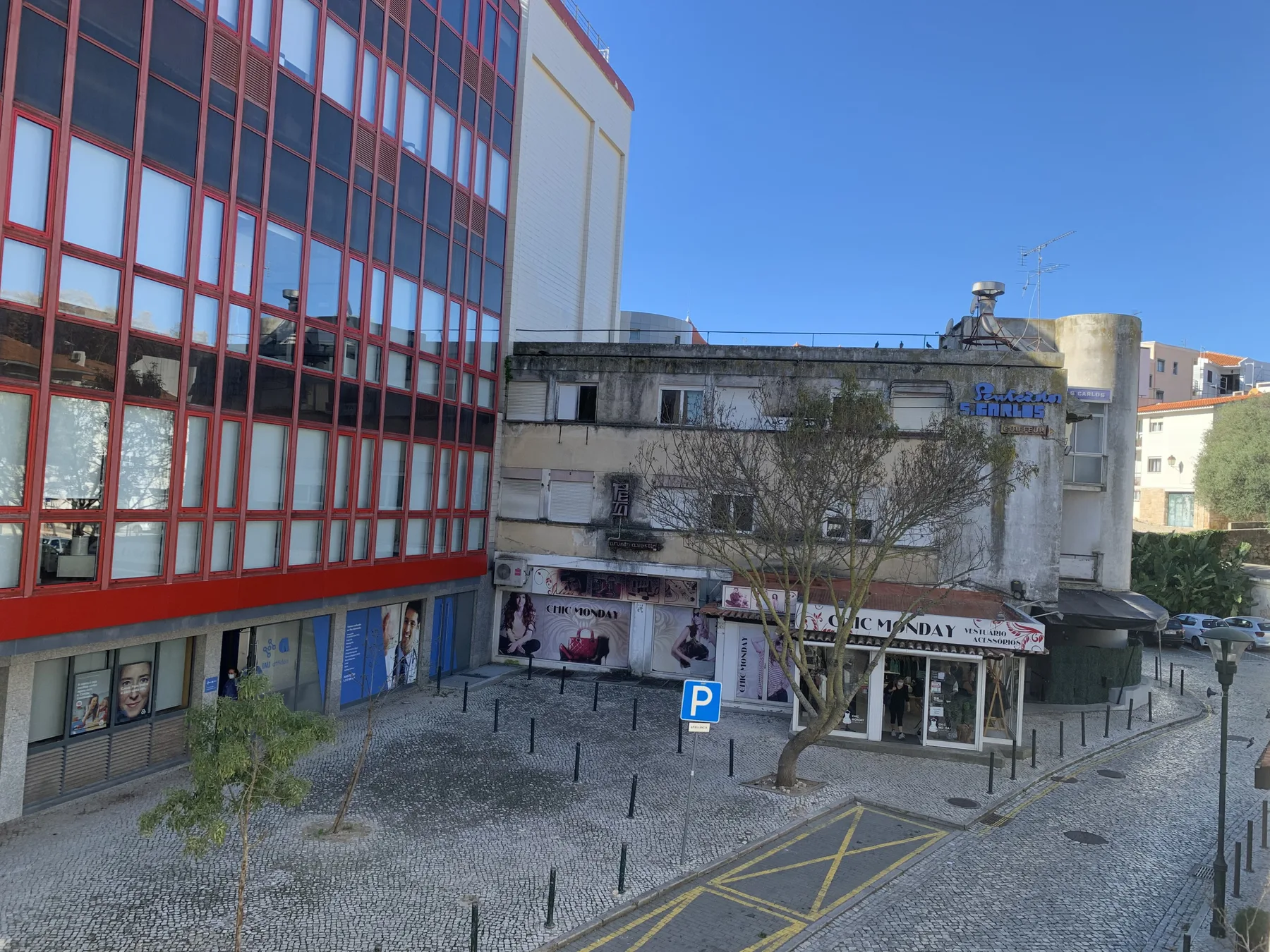 Una calle adoquinada y una pequeña plaza están flanqueadas por tiendas y edificios bajos.
