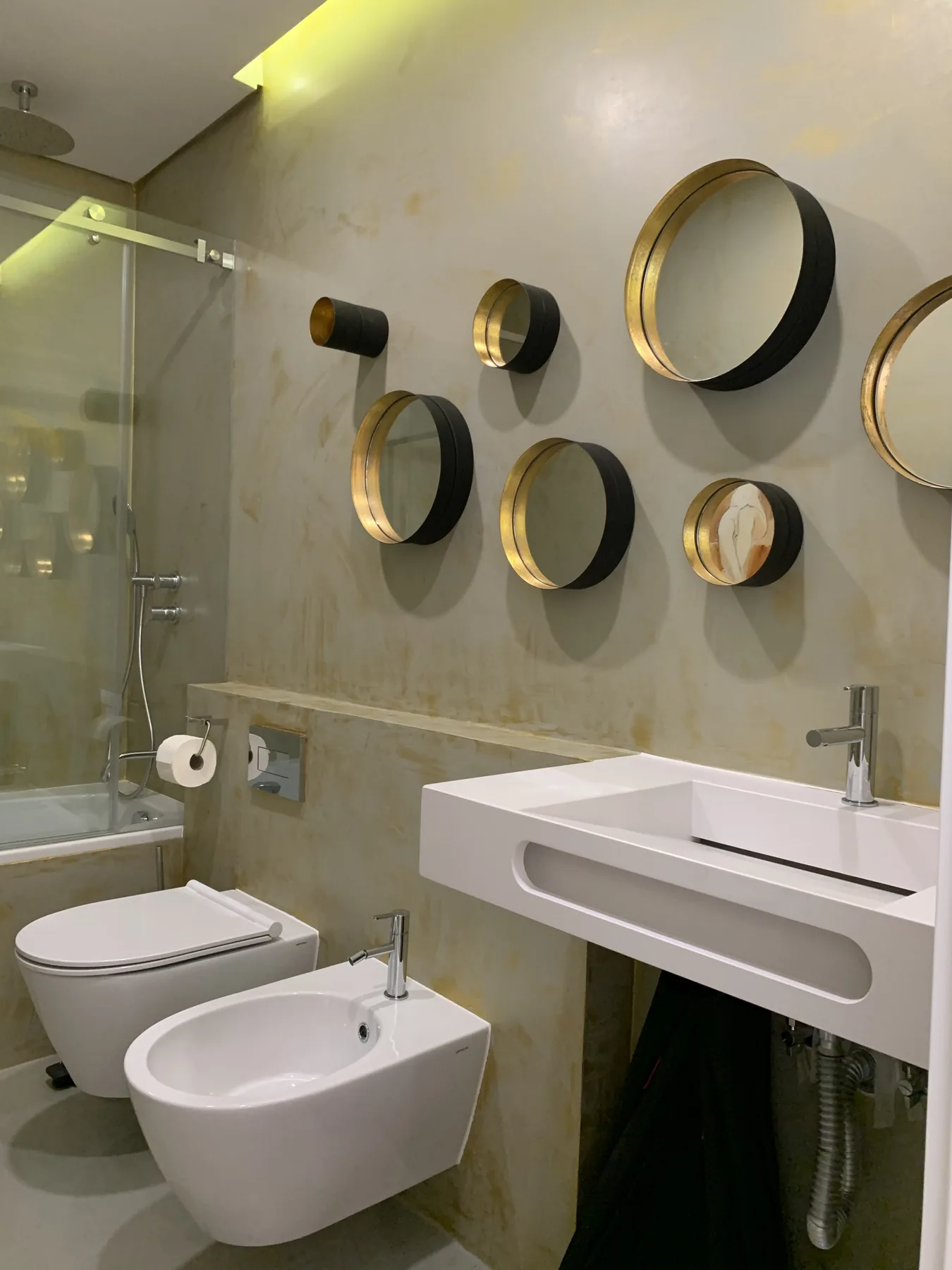Un baño moderno con ducha de cristal y espejos circulares en la pared.