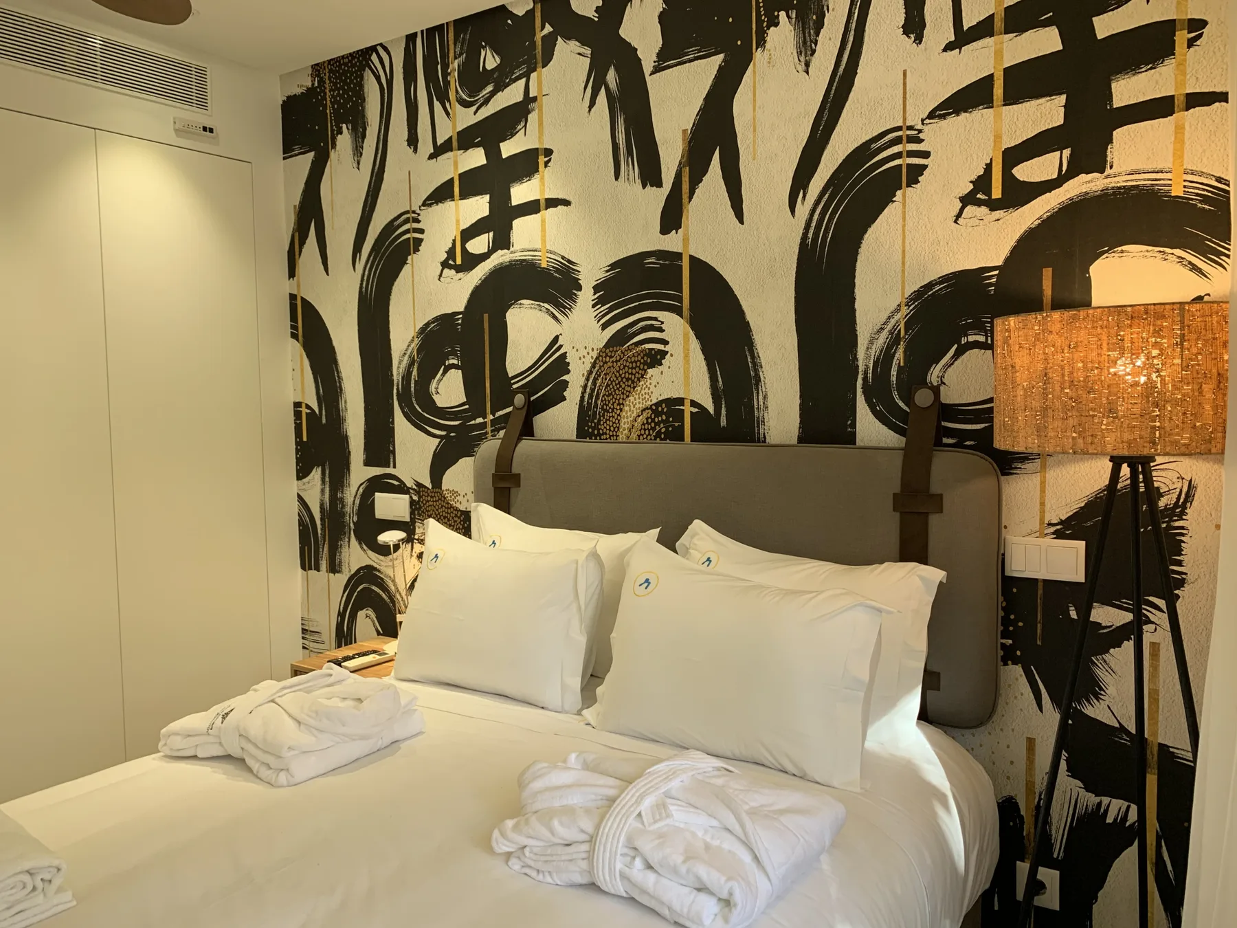 Un dormitorio con ropa de cama blanca y un llamativo mural en negro y crema.