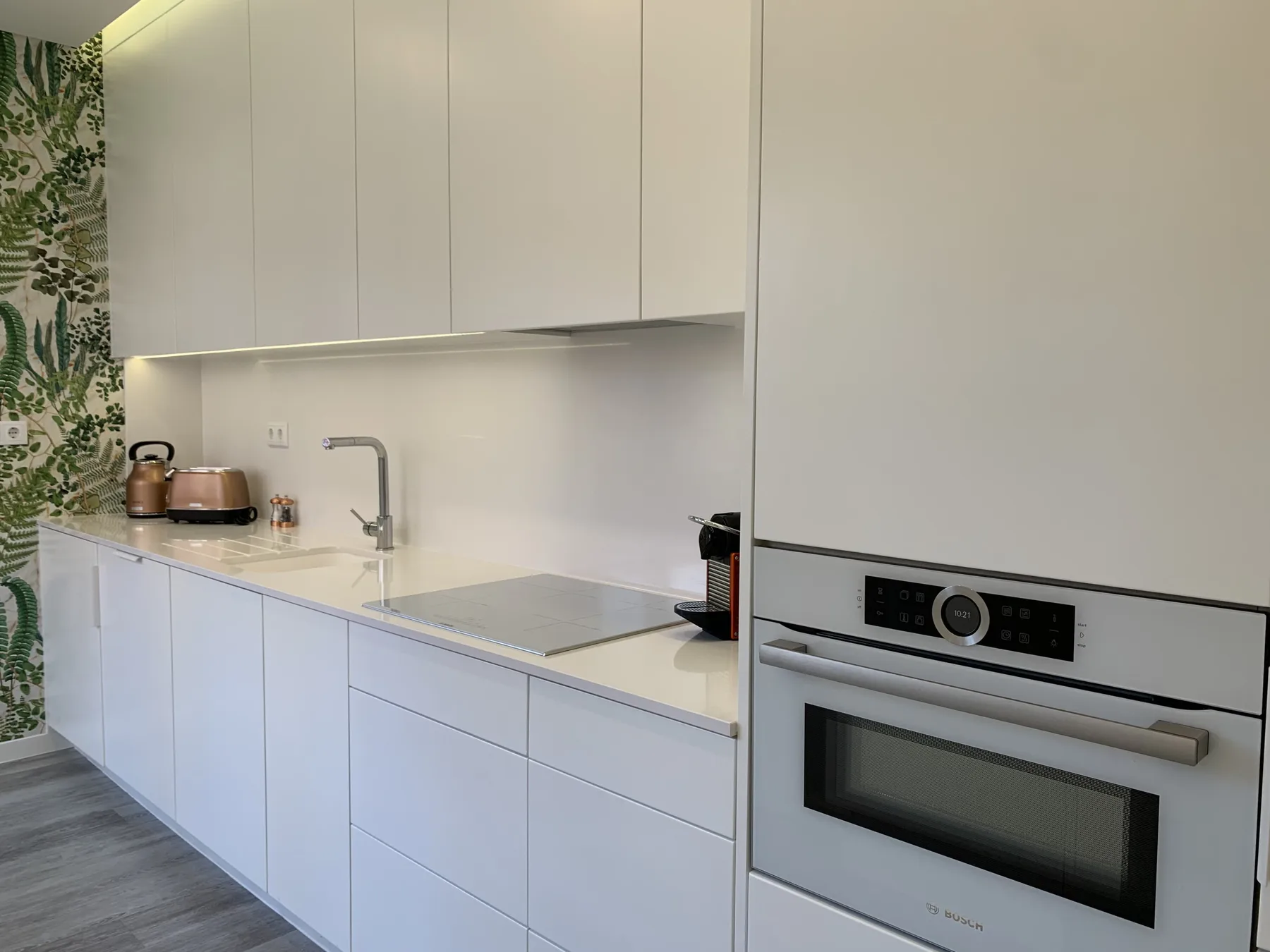 Una cocina moderna con armarios blancos, una placa de cocina y un horno empotrado.