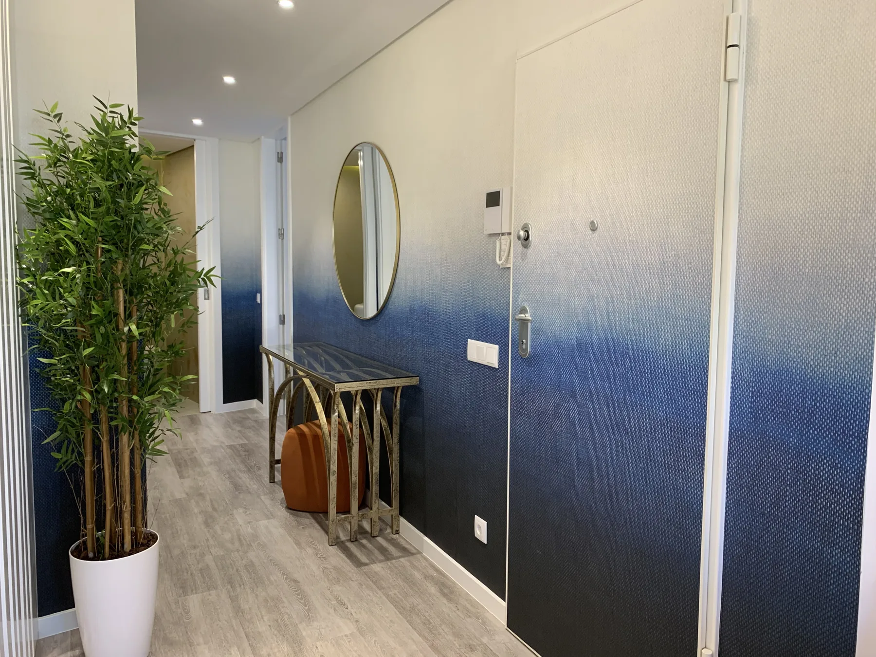 Un recibidor de apartamento con una puerta azul y blanca y un espejo ovalado.