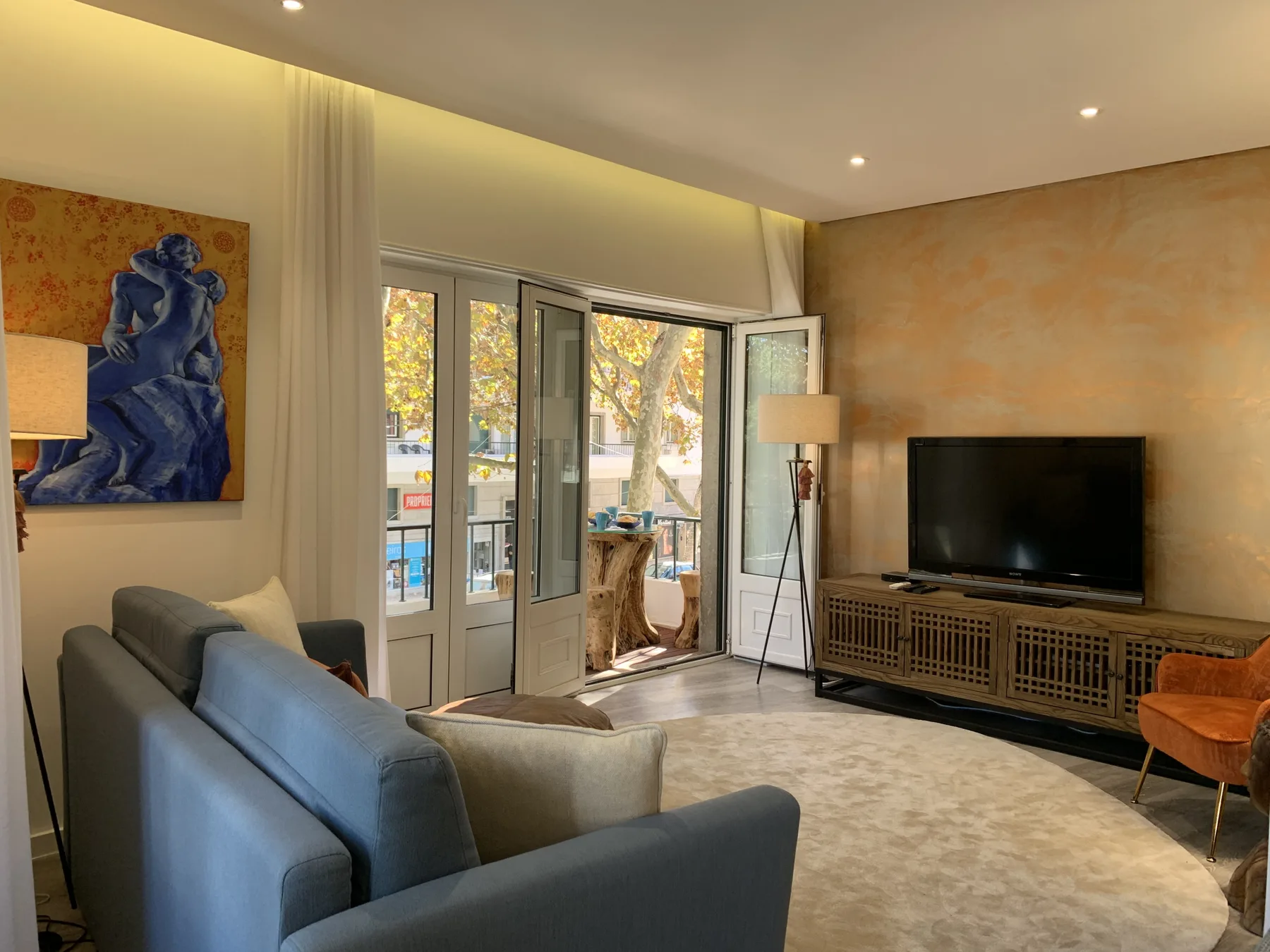 Sala de estar con asientos, televisor y grandes puertas de vidrio que dan a un balcón.
