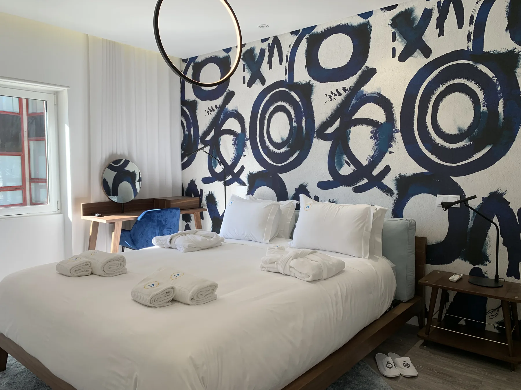 Dormitorio con ropa de cama blanca y un mural abstracto llamativo detrás de la cama.